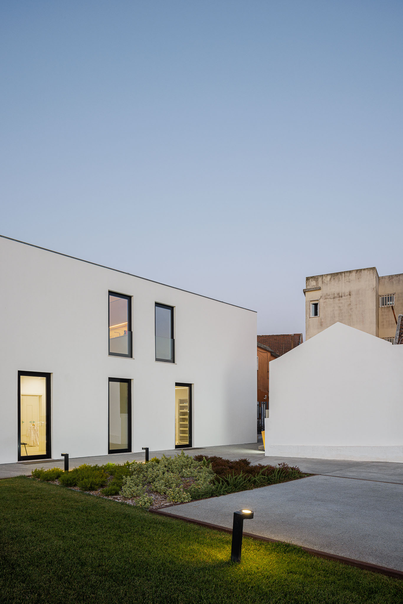 Exterior: Edifício moderno com jardim relvado, iluminação exterior e diferentes volumes arquitetónicos. — Farmácia NR arquitetura Esquissos Arquitectura em Sintra