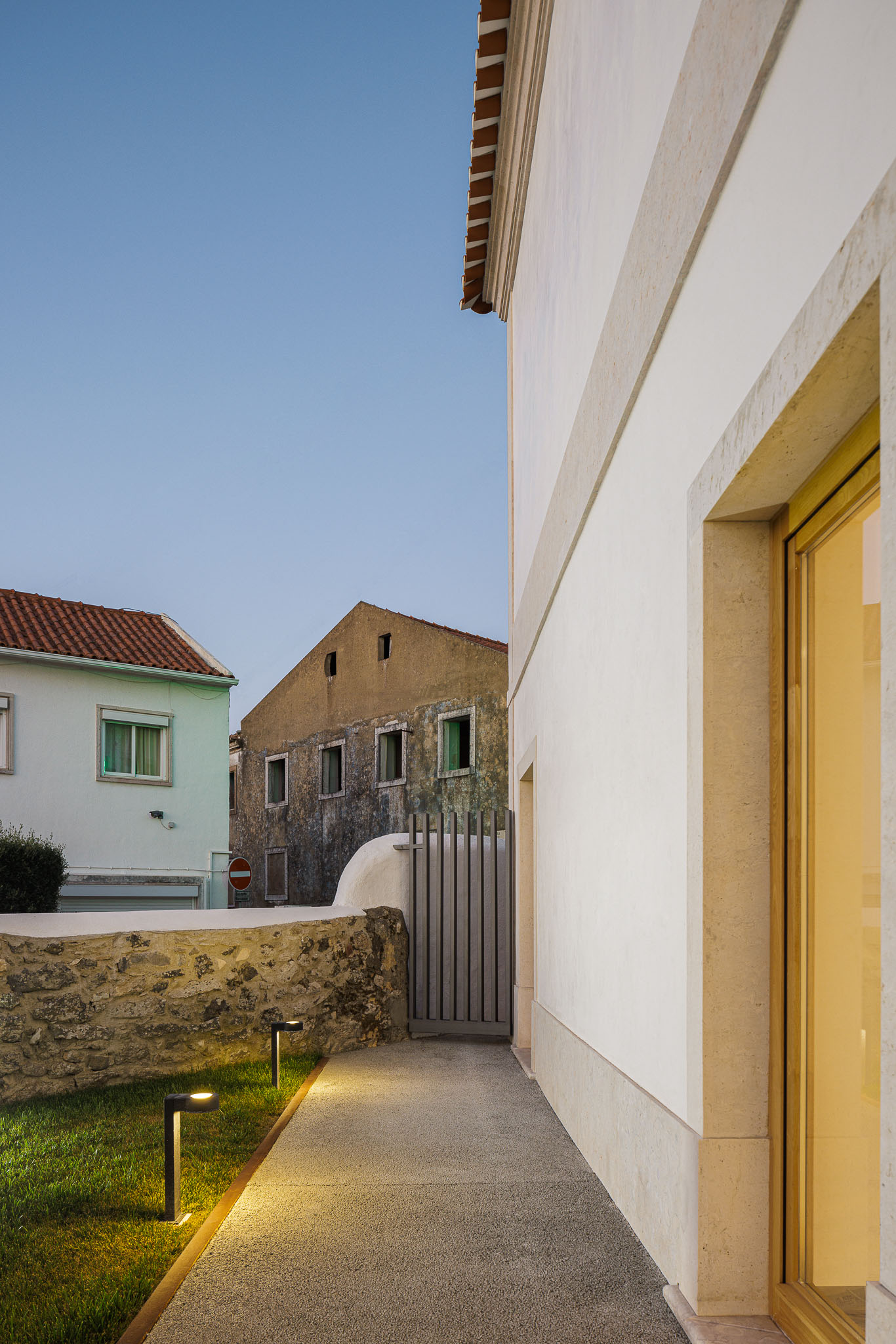 Exterior: Caminho em gravilha com iluminação exterior, muro em pedra e edifício com fachada branca. — Farmácia NR arquitetura Esquissos Arquitectura em Sintra
