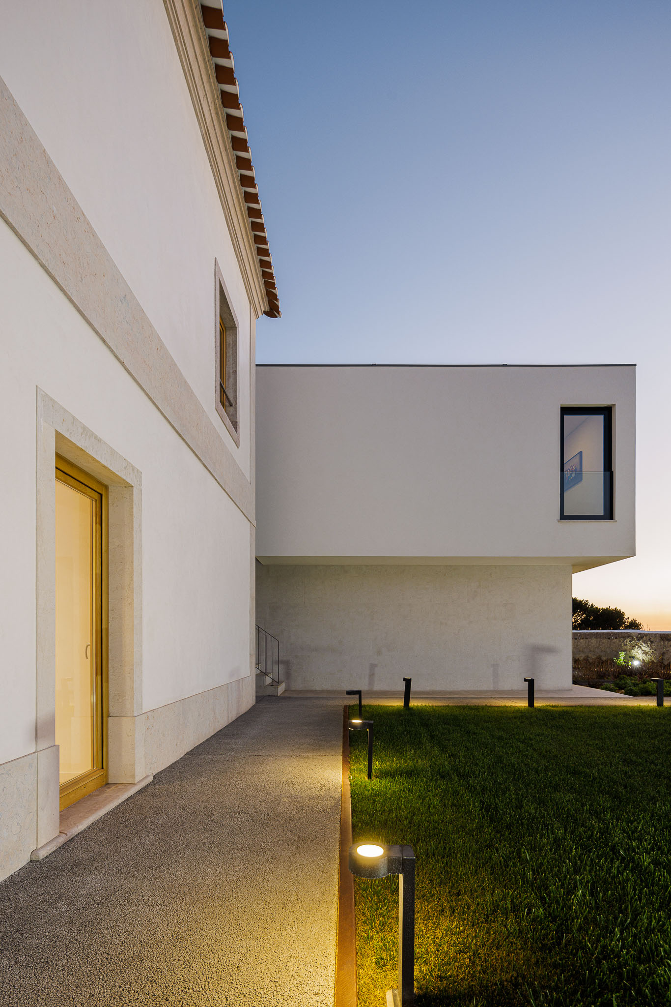 Exterior: Caminho em gravilha com iluminação exterior, jardim relvado e edifícios com arquitetura contrastante. — Farmácia NR arquitetura Esquissos Arquitectura em Sintra