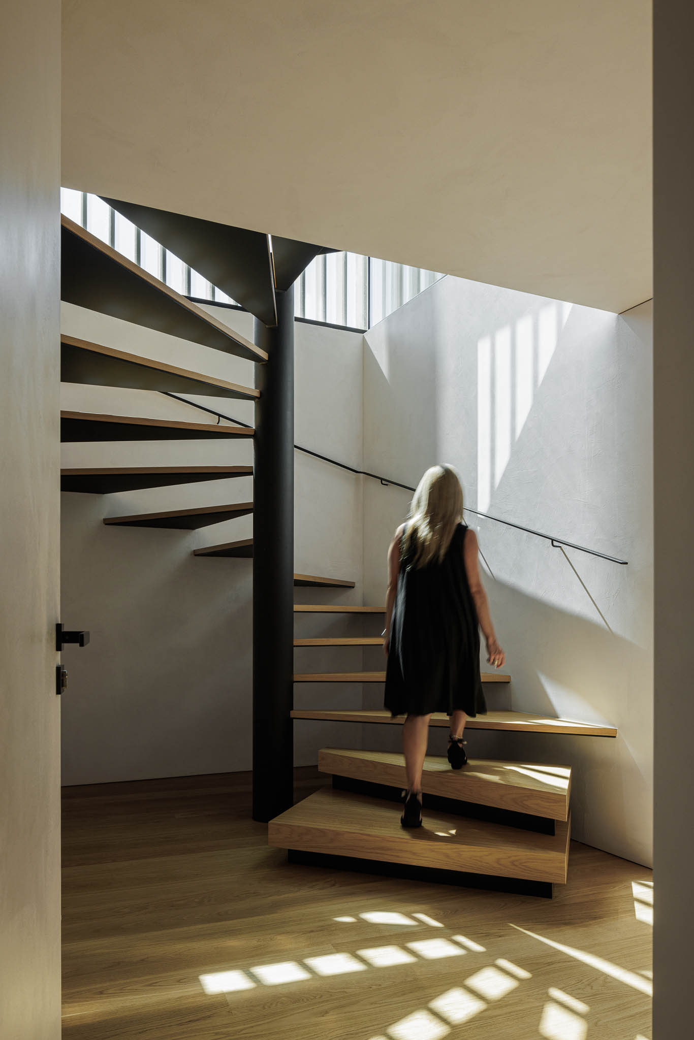 Escadas: Mulher a subir escada em caracol com degraus de madeira e estrutura metálica preta. — Casa de Bouro arquitetura Mutant Architecture and Design em Terras de Bouro