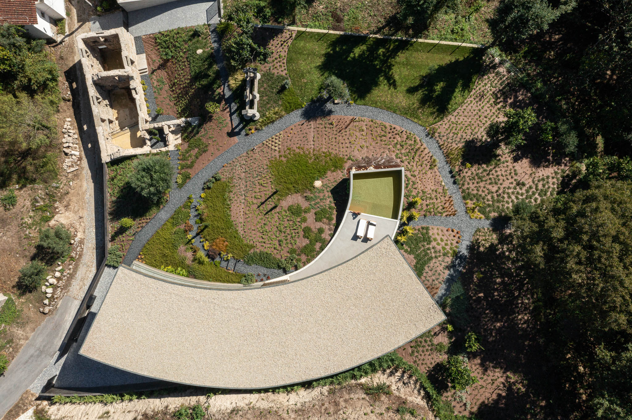 Exterior: Vista aérea da casa com telhado de gravilha, piscina, jardim e ruínas de construção antiga. — Casa de Bouro arquitetura Mutant Architecture and Design em Terras de Bouro