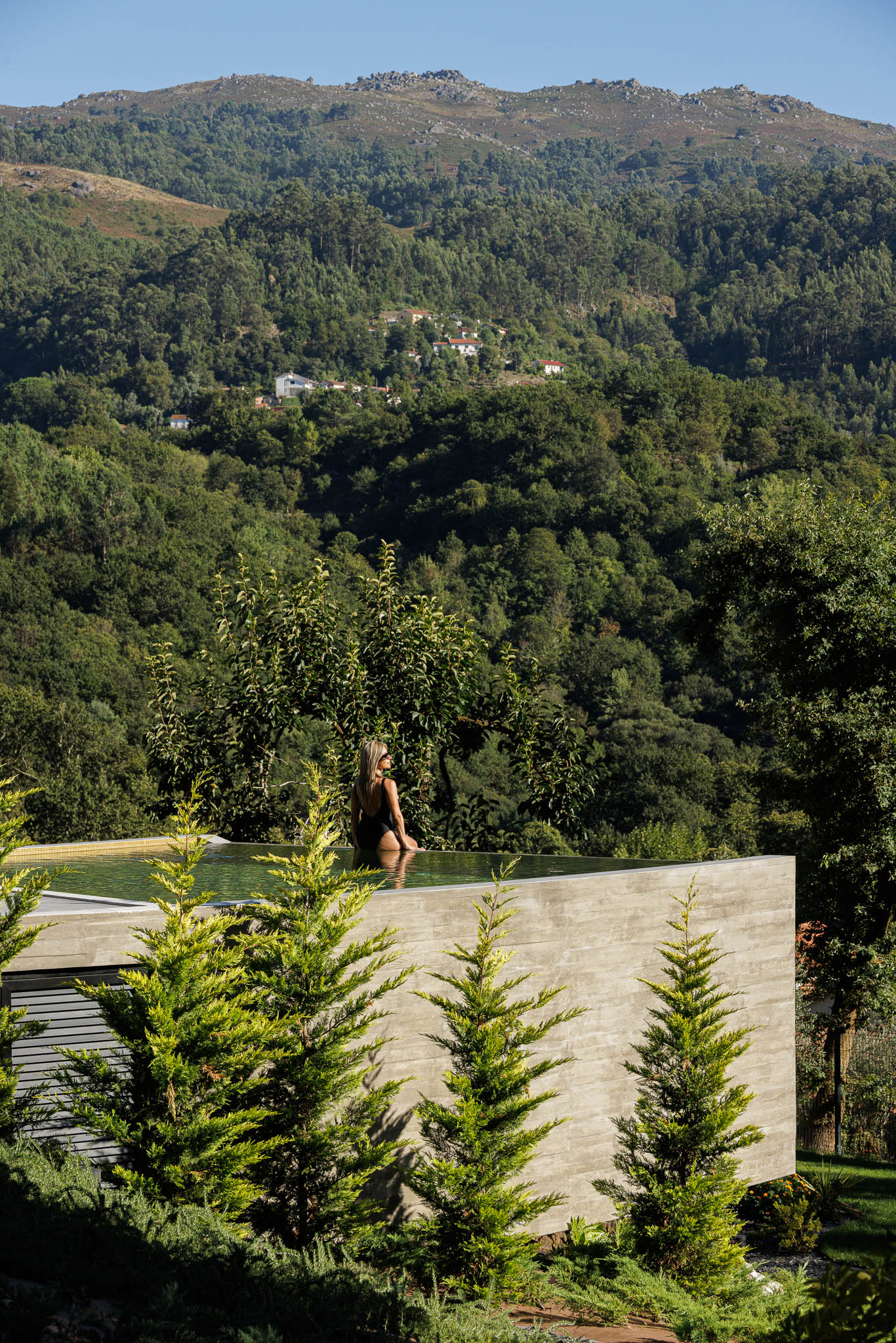 Exterior: Mulher na piscina infinita com vista panorâmica para a montanha e vegetação exuberante. — Casa de Bouro arquitetura Mutant Architecture and Design em Terras de Bouro