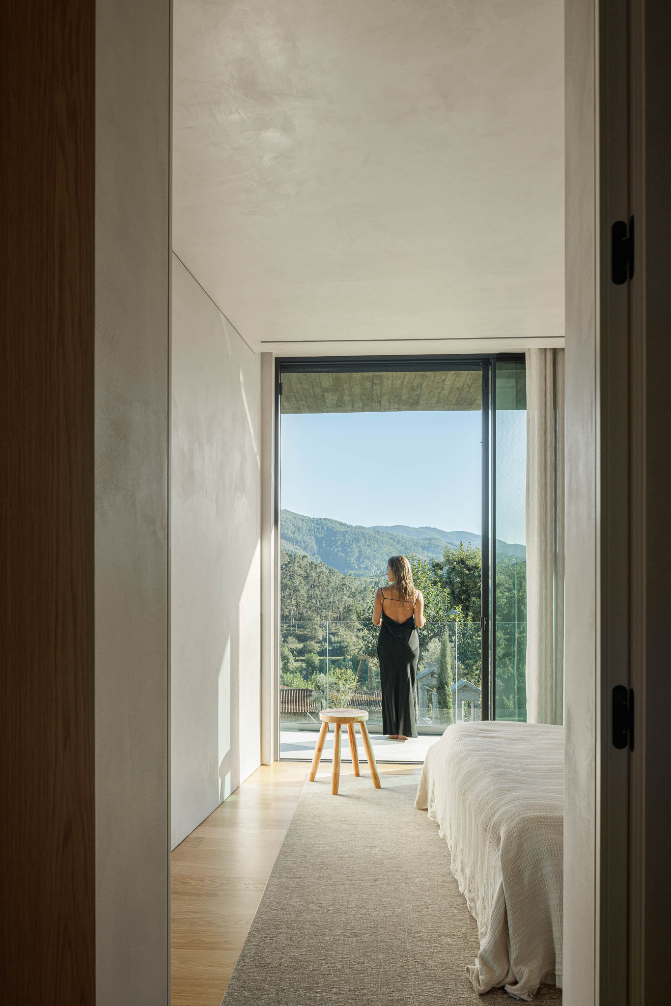 Quarto: Quarto com cama, alcatifa, mesa de cabeceira e porta de correr para a varanda com vista para a montanha. — Casa de Bouro arquitetura Mutant Architecture and Design em Terras de Bouro