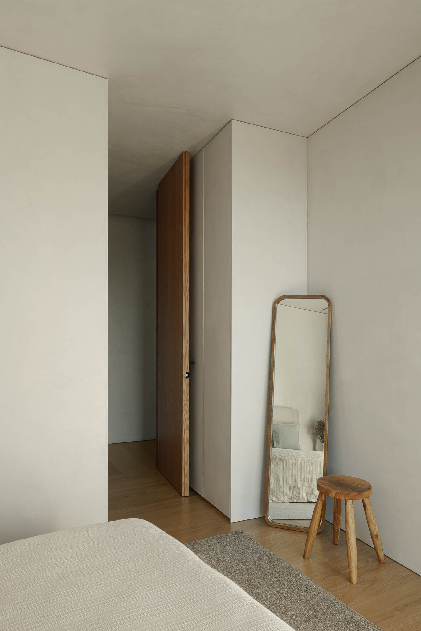 Quarto: Quarto minimalista com espelho de pé, banco de madeira e porta de madeira. — Casa de Bouro arquitetura Mutant Architecture and Design em Terras de Bouro