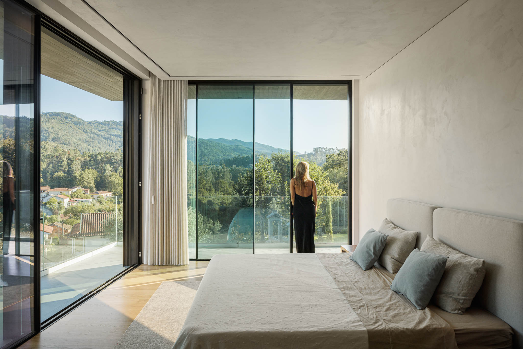 Quarto: Quarto com cama de casal, grandes janelas panorâmicas e vista para a paisagem natural. — Casa de Bouro arquitetura Mutant Architecture and Design em Terras de Bouro