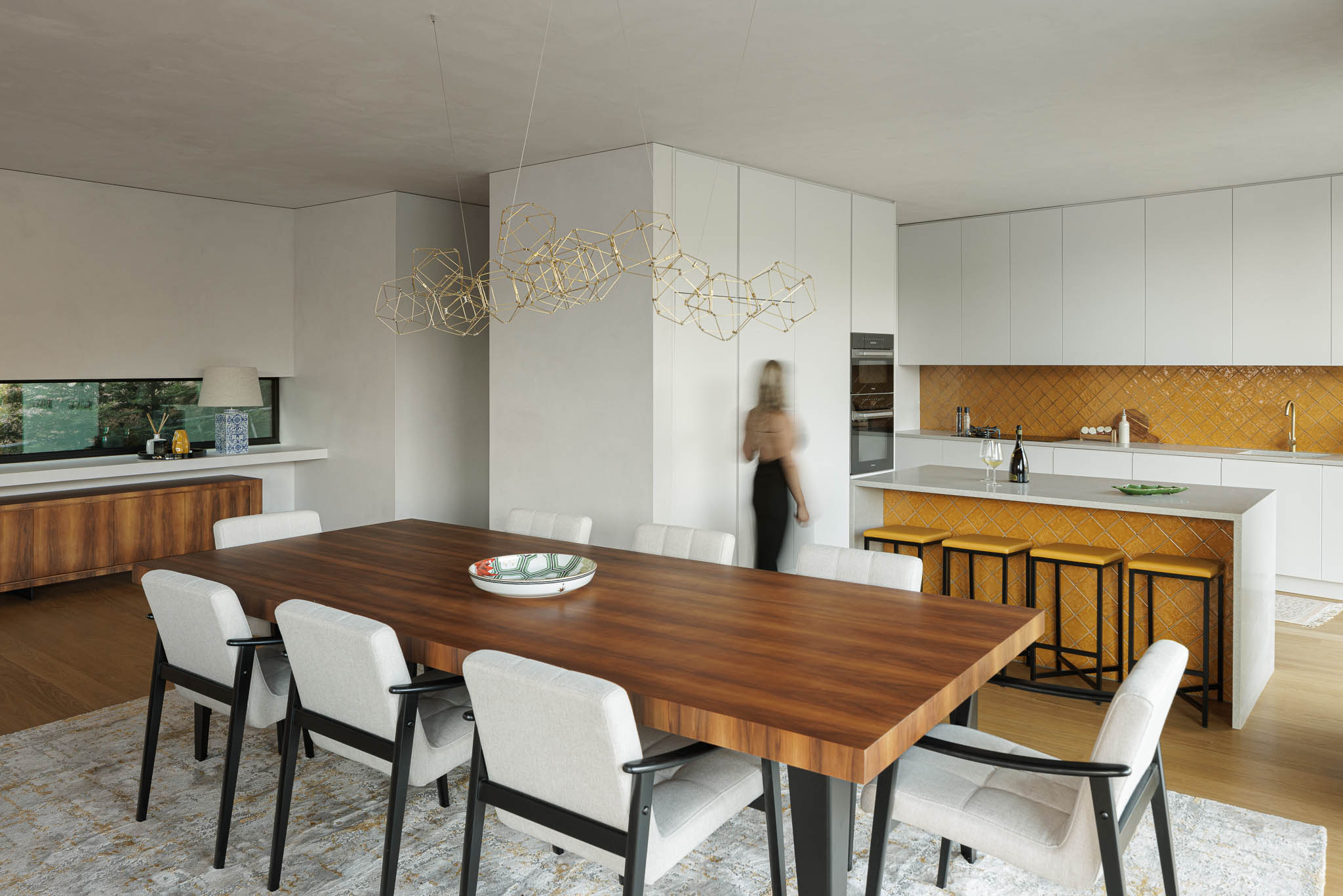Cozinha/Sala de jantar: Espaço amplo com cozinha branca, ilha com azulejos amarelos e mesa de jantar em madeira. — Casa de Bouro arquitetura Mutant Architecture and Design em Terras de Bouro