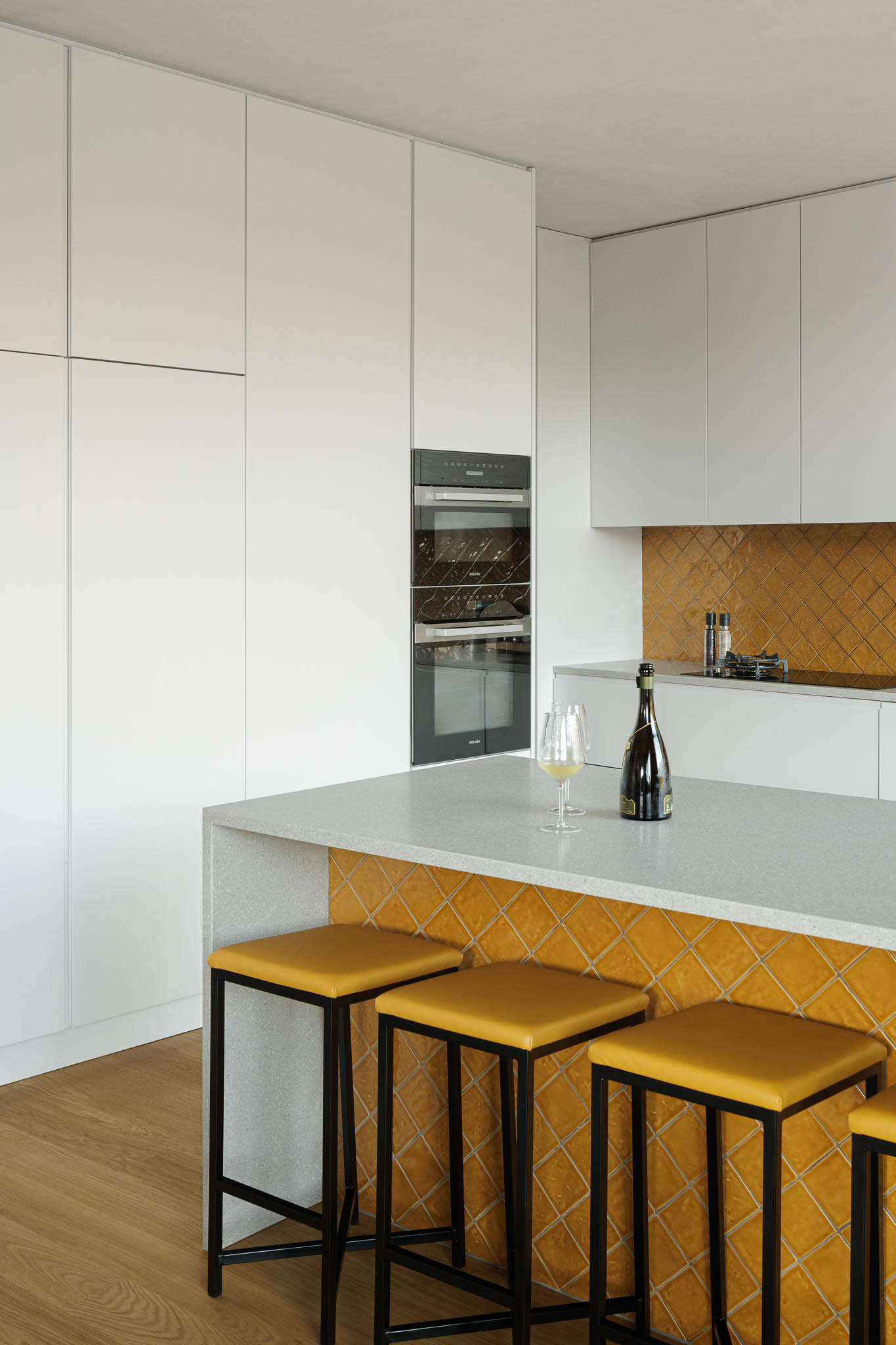 Cozinha: Detalhe da ilha da cozinha com azulejos amarelos, bancada em pedra e armários brancos. — Casa de Bouro arquitetura Mutant Architecture and Design em Terras de Bouro