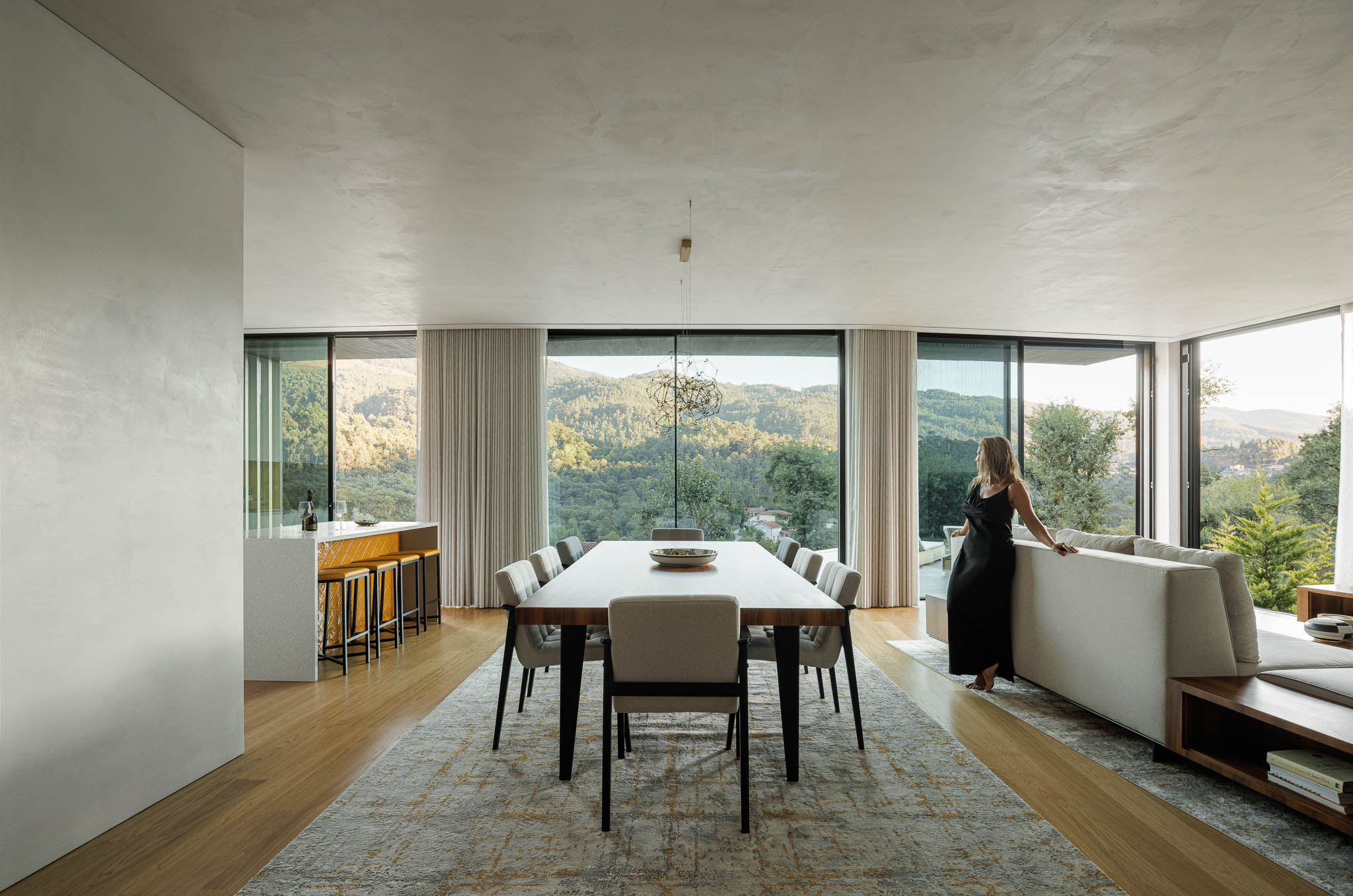 Sala de estar/Jantar: Espaço amplo com sala de estar, mesa de jantar e cozinha, com vista panorâmica para a montanha. — Casa de Bouro arquitetura Mutant Architecture and Design em Terras de Bouro