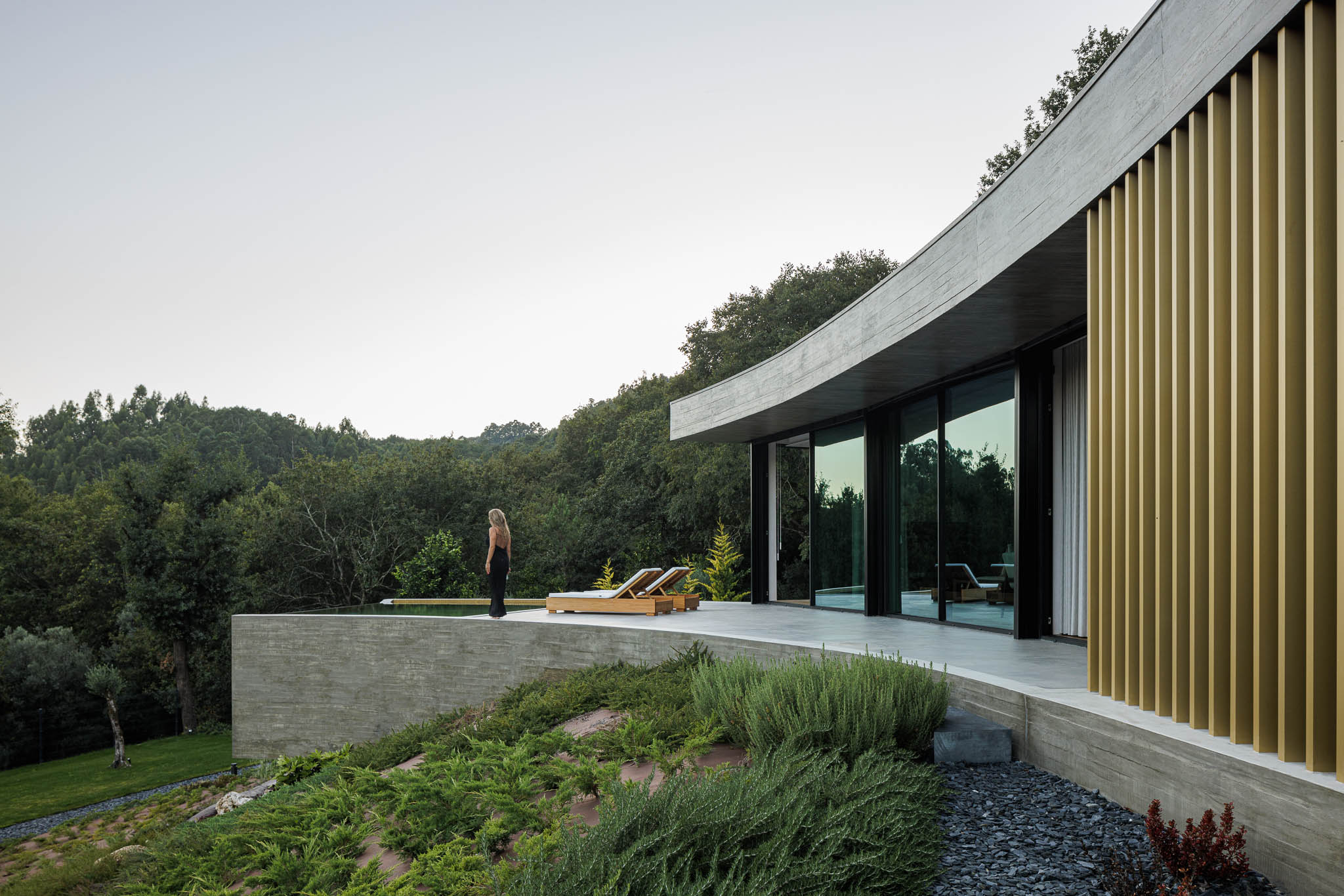 Exterior: Varanda curva com vista para a paisagem natural, piscina e jardim em socalcos. — Casa de Bouro arquitetura Mutant Architecture and Design em Terras de Bouro