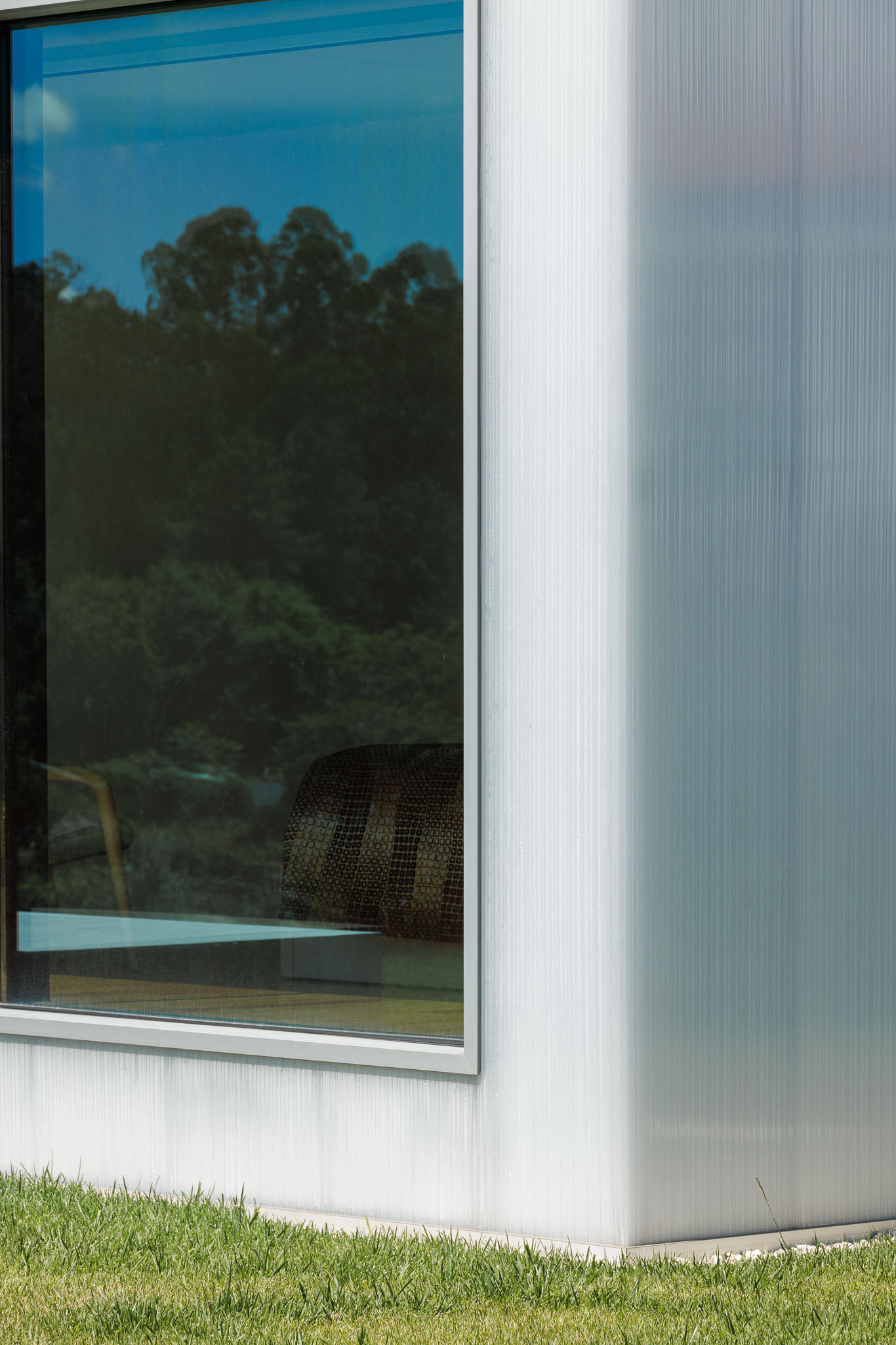 Fachada: Detalhe do revestimento translúcido e janela com caixilharia metálica. Reflexo da vegetação no vidro. — Casa Ponte arquitetura stu.dere em Amarante