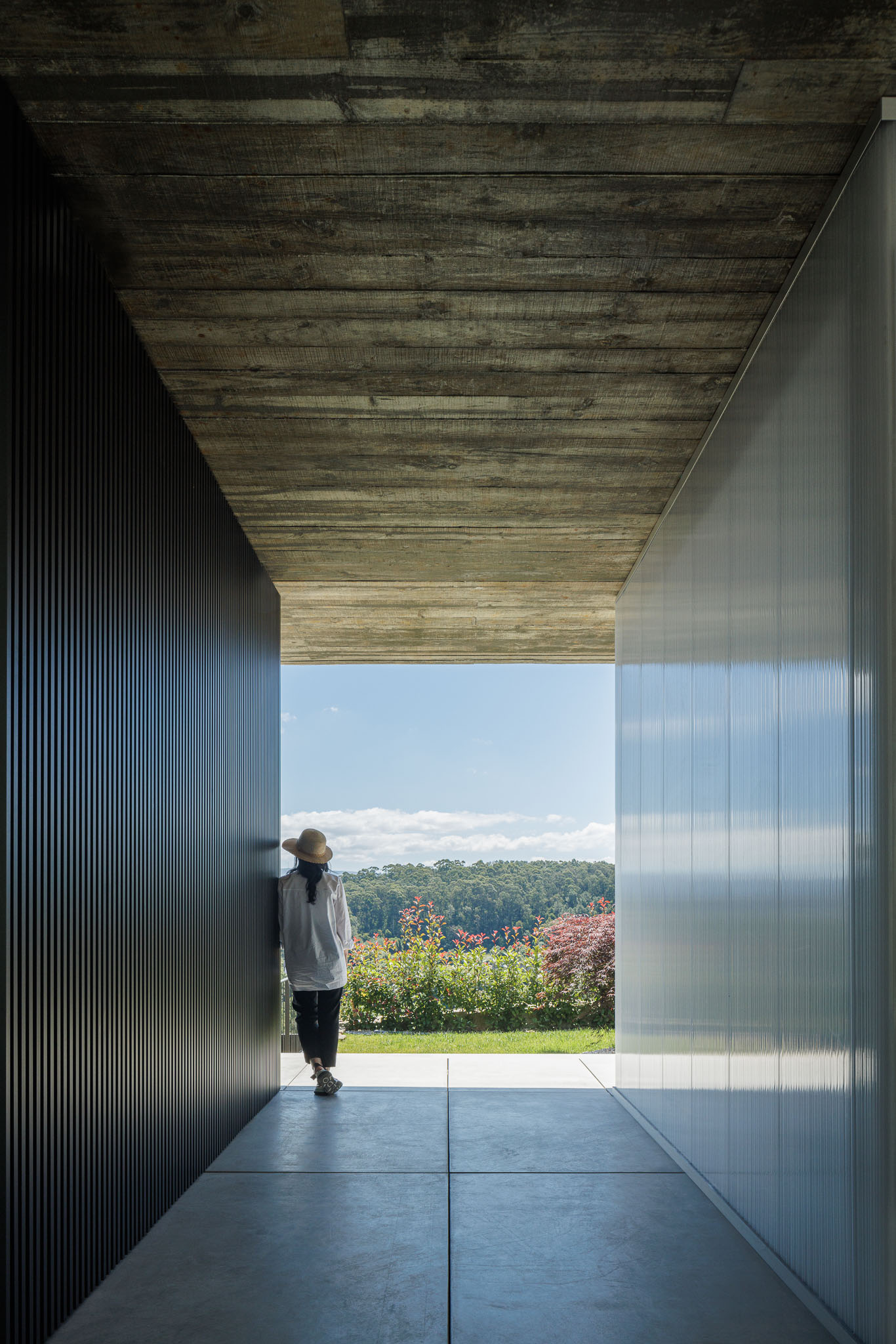 Circulação: Corredor com paredes revestidas a madeira escura e material translúcido. Pavimento em betão e vista para o exterior. — Casa Ponte arquitetura stu.dere em Amarante