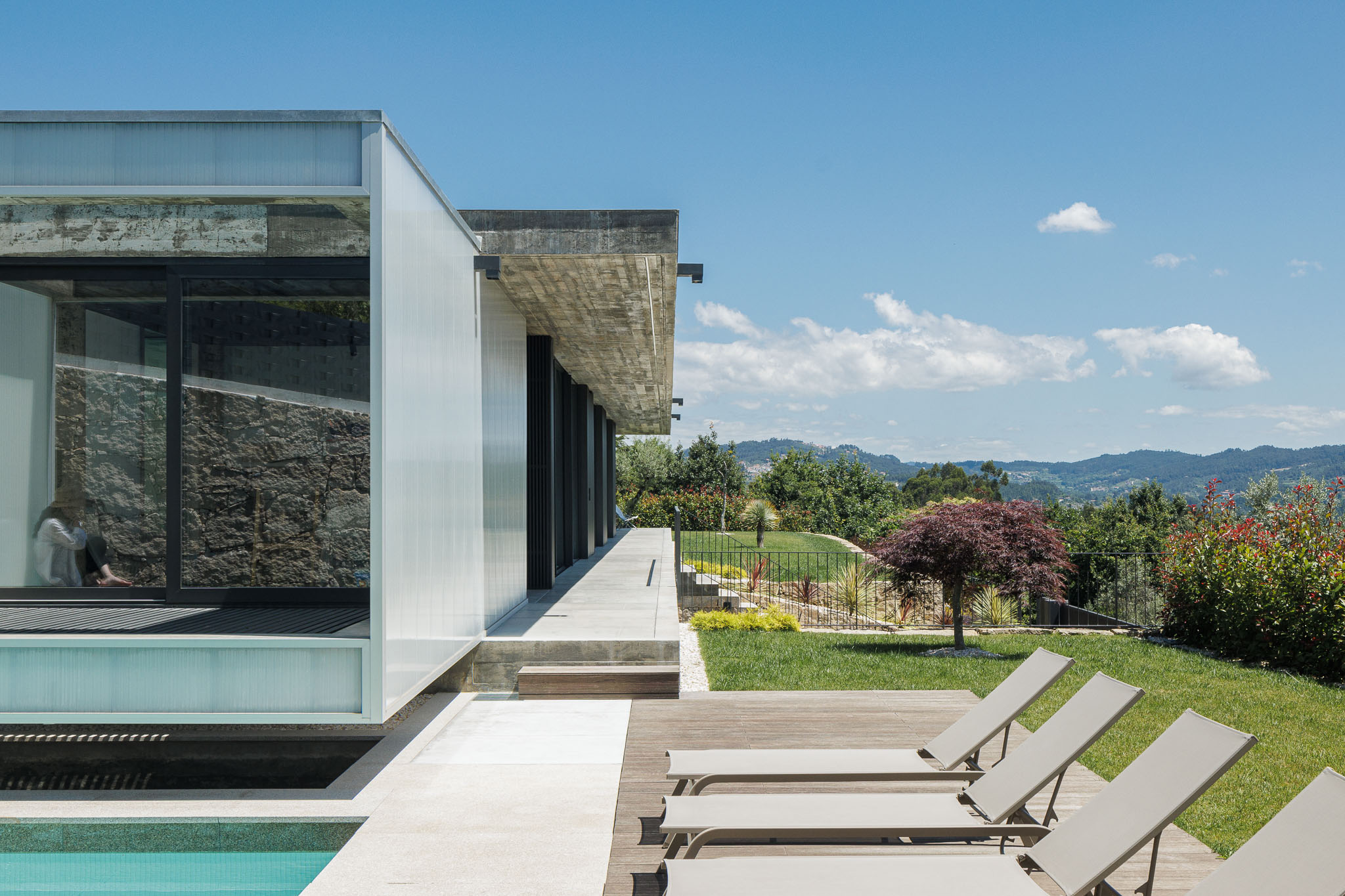 Exterior: Piscina e zona de lazer com espreguiçadeiras. Revestimento translúcido na fachada e teto em betão aparente. — Casa Ponte arquitetura stu.dere em Amarante