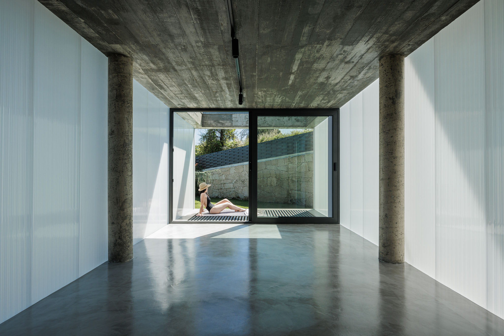 Piscina interior: Espaço com paredes translúcidas, teto em betão aparente e pavimento em betão polido. Pessoa a relaxar. — Casa Ponte arquitetura stu.dere em Amarante