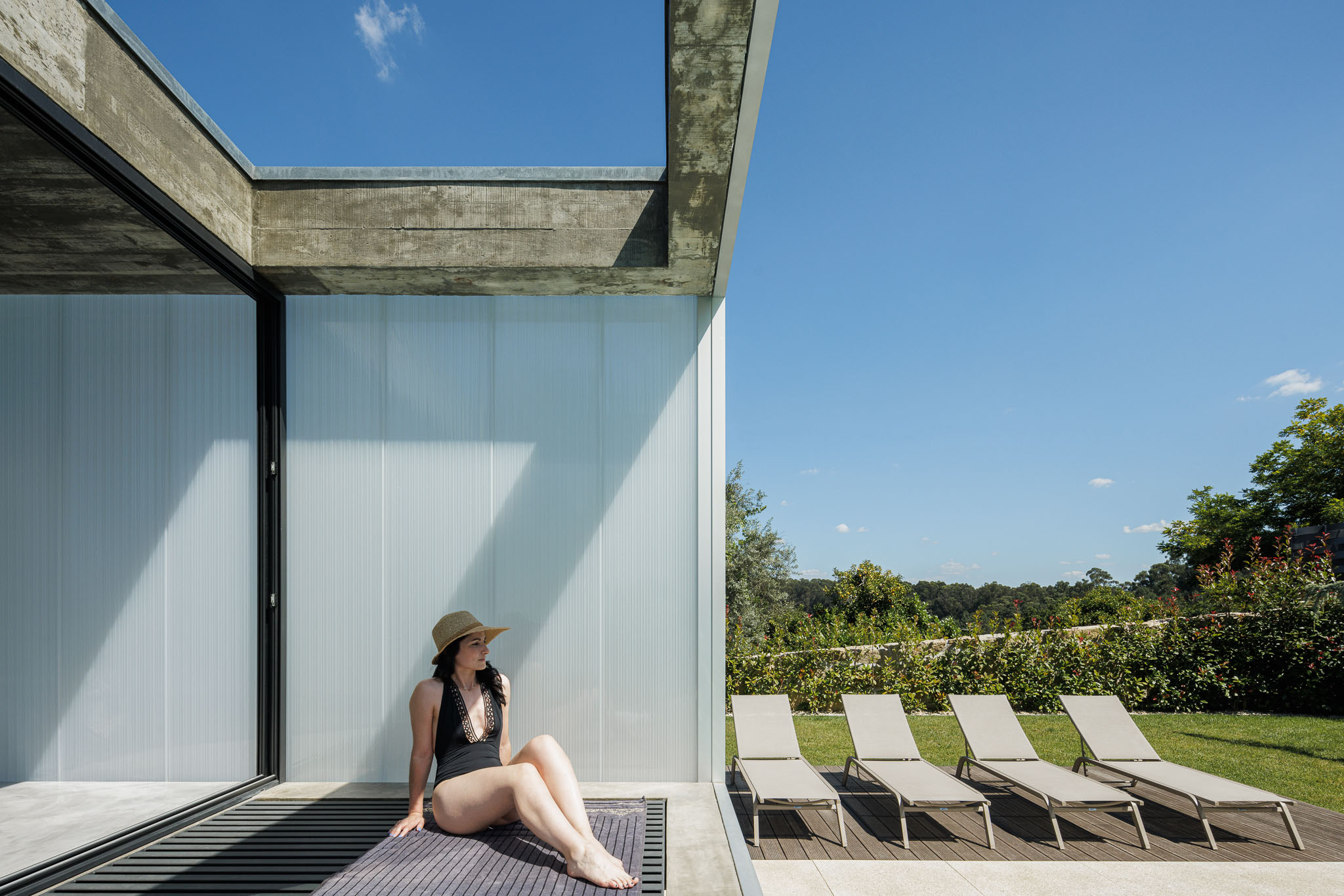 Exterior: Zona da piscina com espreguiçadeiras e relvado. Revestimento translúcido na fachada da casa. — Casa Ponte arquitetura stu.dere em Amarante