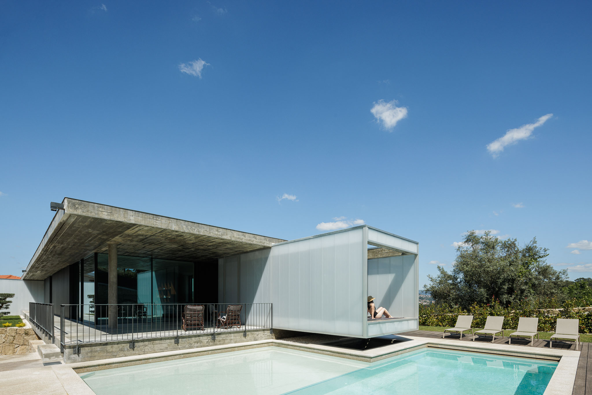 Exterior: Vista da casa a partir da piscina, com zona de estar exterior e revestimento translúcido. — Casa Ponte arquitetura stu.dere em Amarante