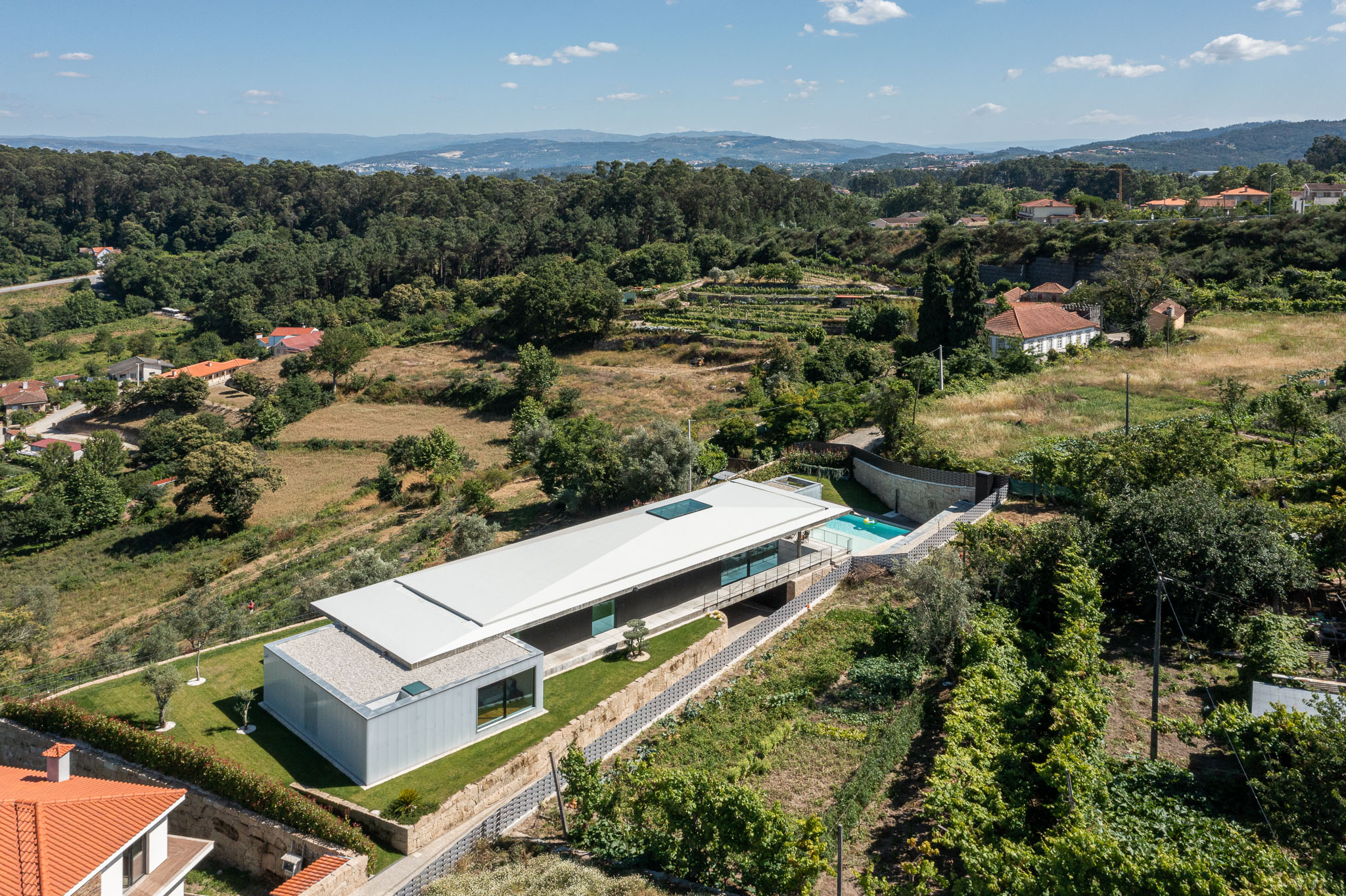 Exterior: Vista aérea da casa integrada na paisagem rural, com piscina e telhado branco. — Casa Ponte arquitetura stu.dere em Amarante