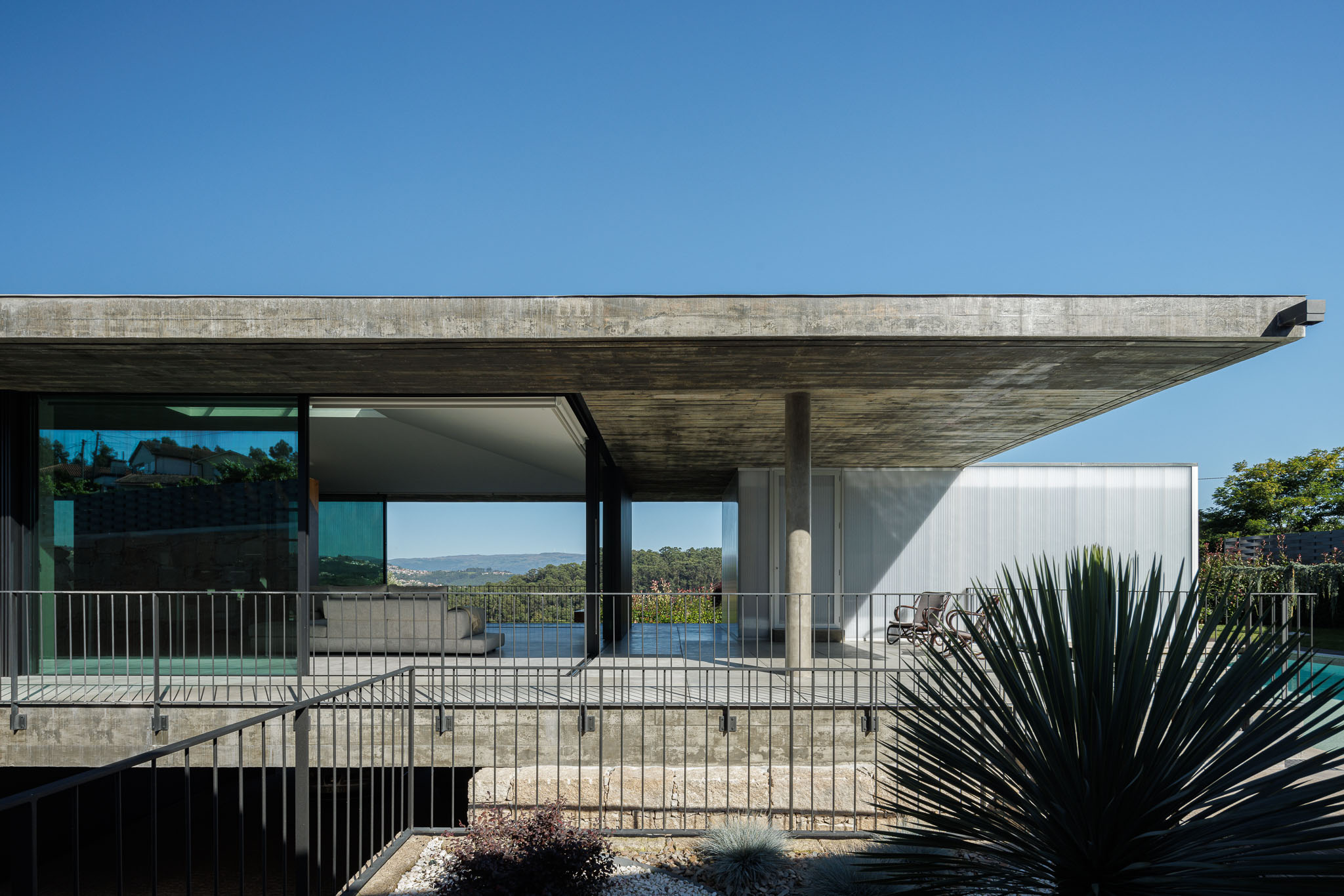 Varanda: Vista da varanda com guarda corpo metálico, teto em betão e acesso à piscina. — Casa Ponte arquitetura stu.dere em Amarante