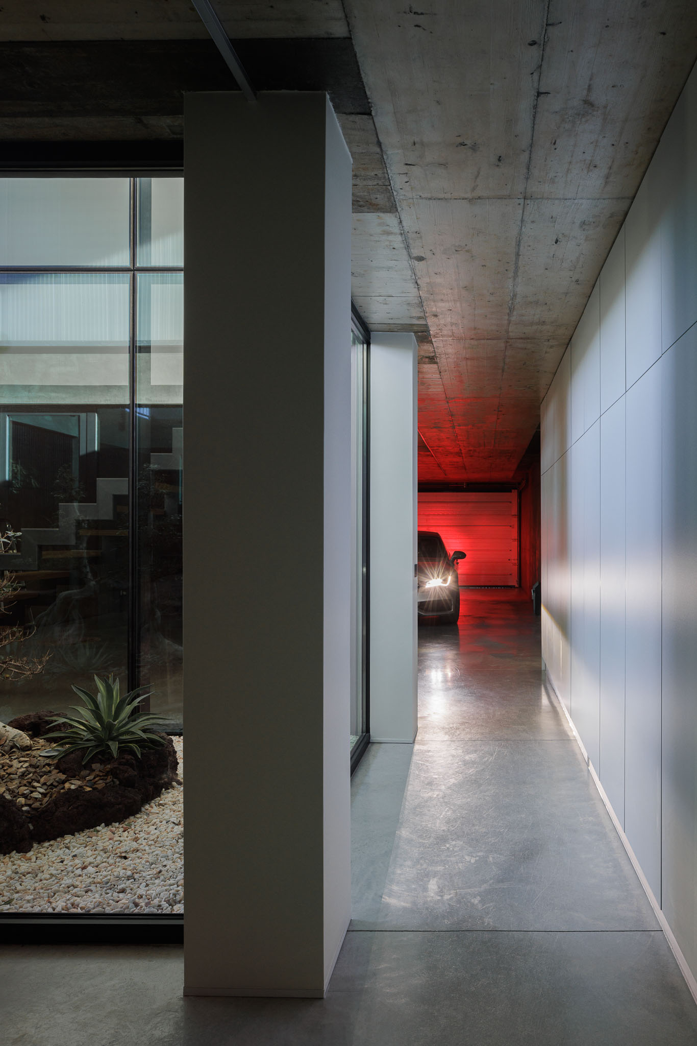 Corredor: Corredor com armários embutidos, pavimento em betão e acesso à garagem. — Casa Ponte arquitetura stu.dere em Amarante