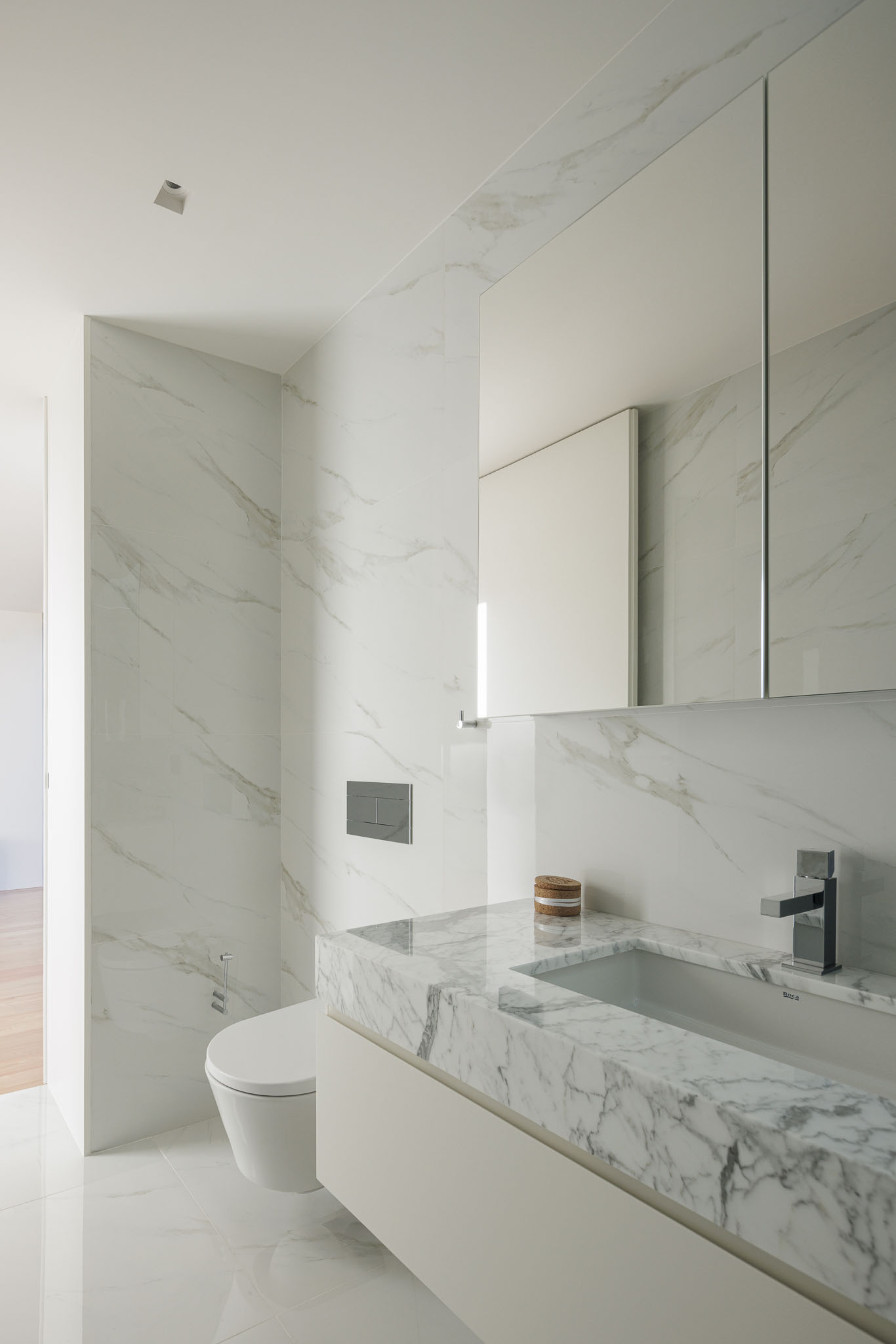 Casa de banho: Revestimento em mármore branco, lavatório embutido e sanita suspensa. — Casa Ponte arquitetura stu.dere em Amarante