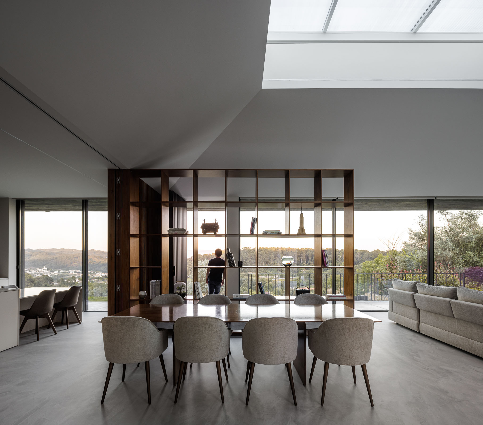 Sala de jantar: Mesa de jantar com cadeiras cinzentas, estante em madeira e vista panorâmica. — Casa Ponte arquitetura stu.dere em Amarante