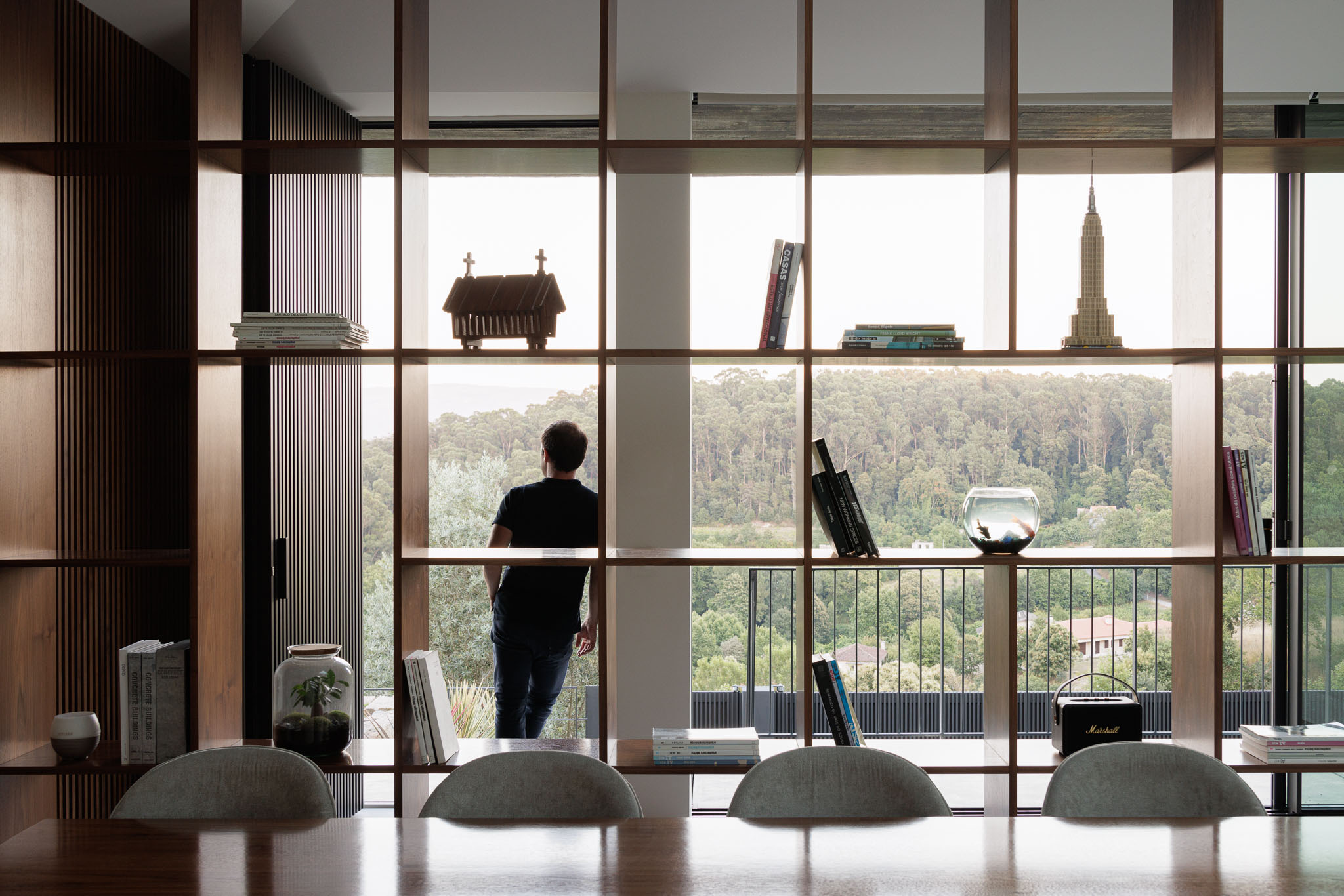 Sala de jantar: Detalhe da estante em madeira com objetos decorativos e vista para a paisagem. — Casa Ponte arquitetura stu.dere em Amarante