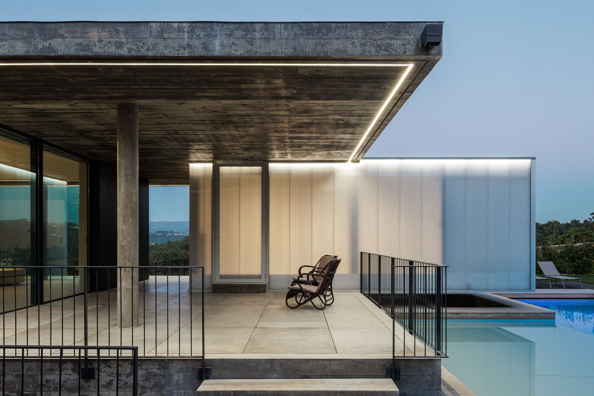 Exterior: Zona de estar exterior com cadeiras de baloiço, teto em betão e revestimento translúcido. Piscina em primeiro plano. — Casa Ponte arquitetura stu.dere em Amarante