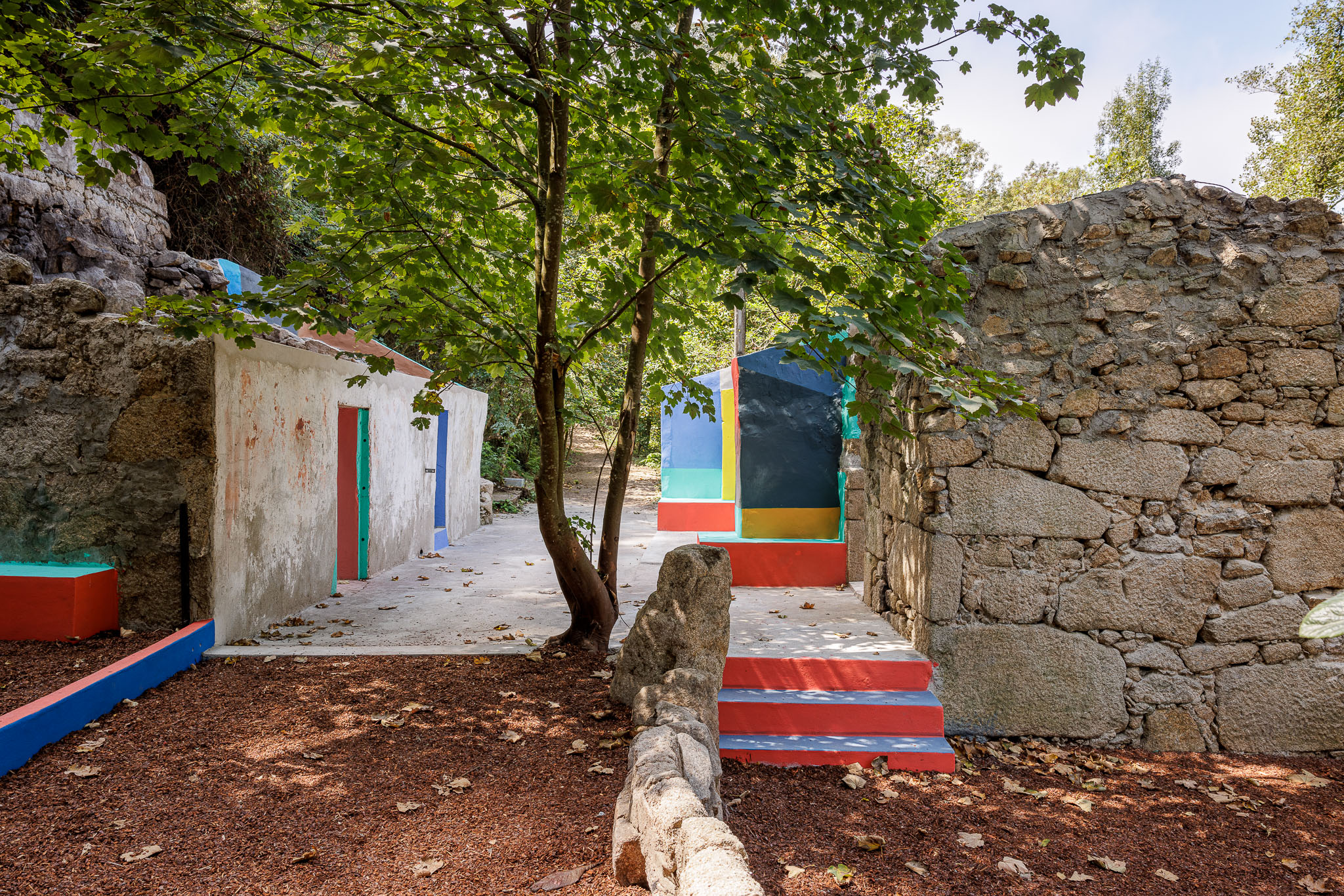Espaço de lazer: Ruínas de pedra e estruturas coloridas em betão pintado, num parque com pavimento de madeira lascada. — Caminho das Escadinhas arquitetura Paulo Moreira Architectures e verkron em Matosinhos