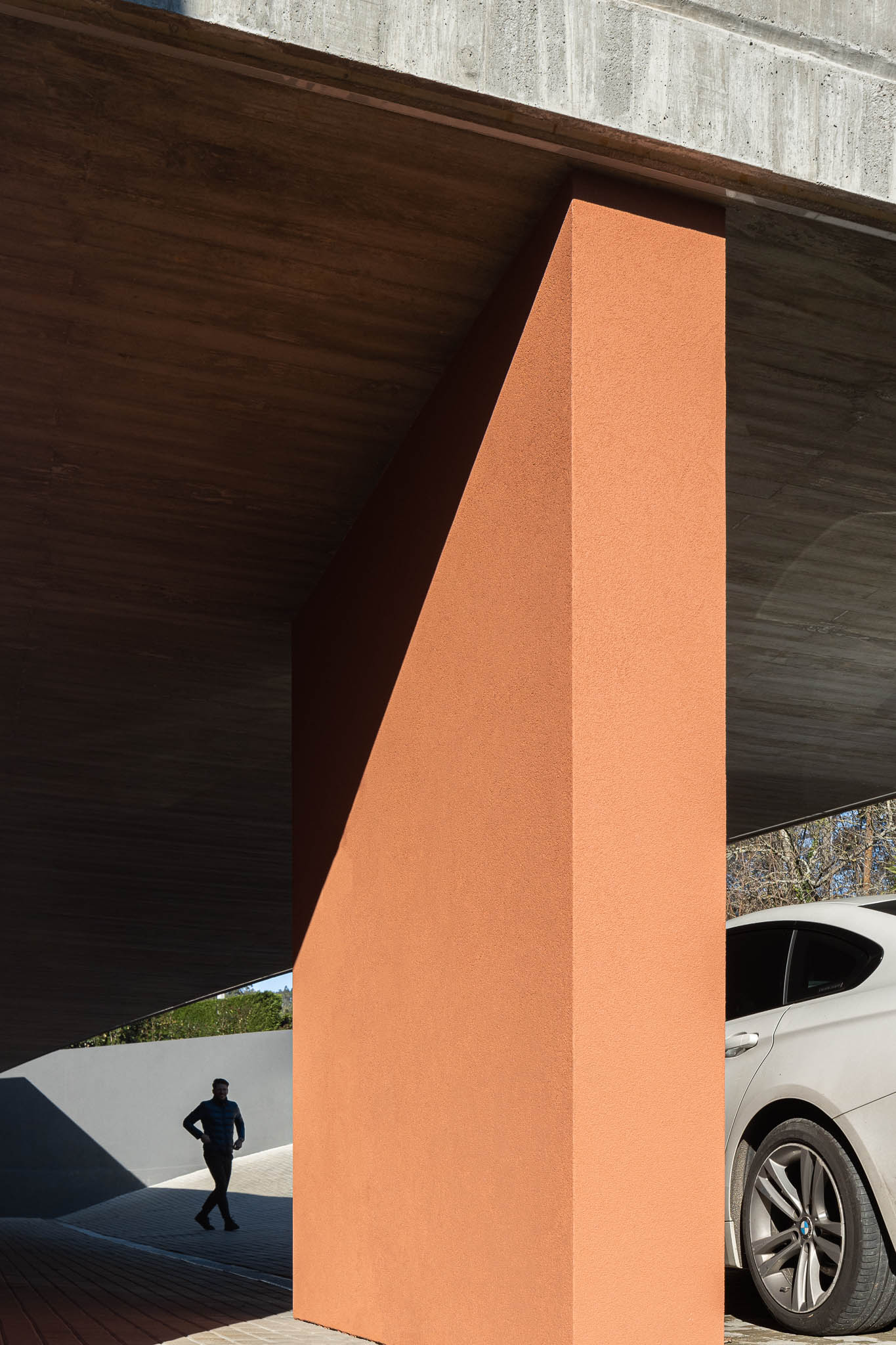 Alpendre: Pilar cor de tijolo sob laje de betão aparente, pavimento em calçada. Homem a caminhar. — TM House arquitetura Inception Architects Studio em Santo Tirso