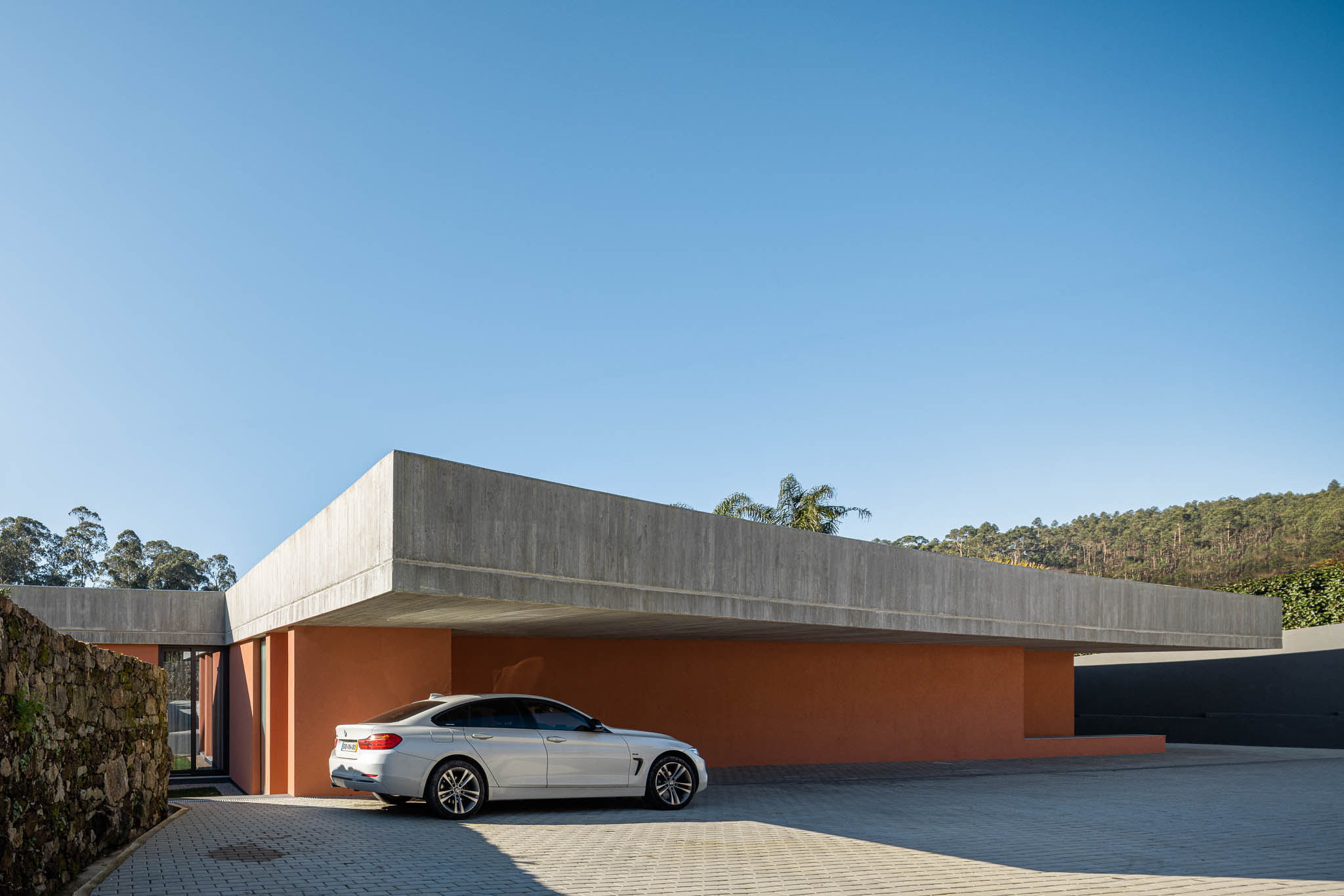 Exterior: Vista geral da casa com laje de betão aparente e paredes cor de tijolo. Carro estacionado. — TM House arquitetura Inception Architects Studio em Santo Tirso