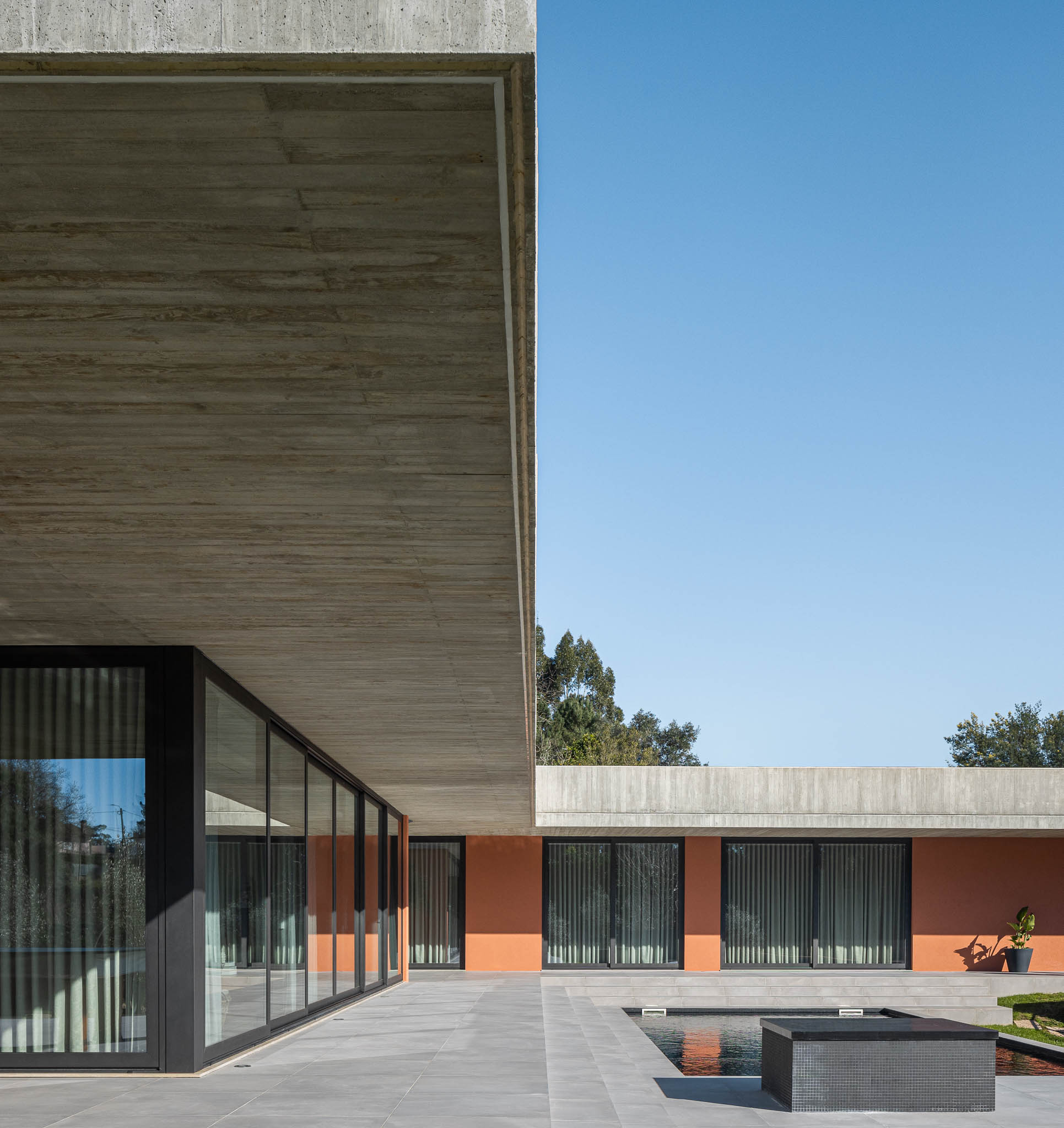 Exterior: Alpendre com laje de betão aparente e paredes cor de tijolo, grandes janelas. — TM House arquitetura Inception Architects Studio em Santo Tirso