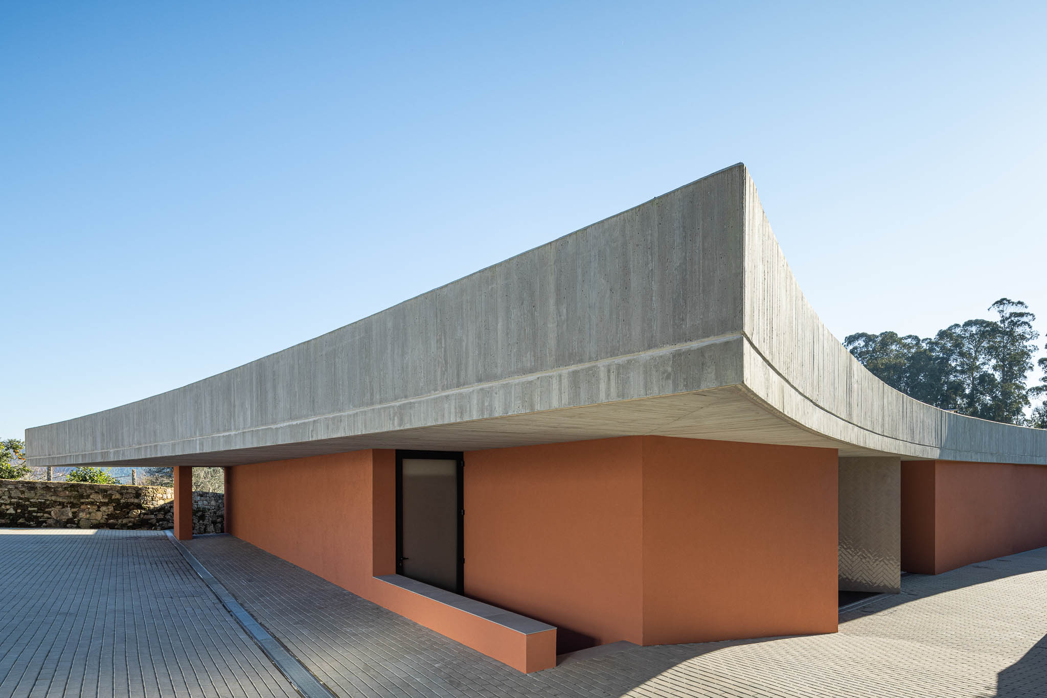 Exterior: Laje de betão aparente com forma curva e paredes cor de tijolo. — TM House arquitetura Inception Architects Studio em Santo Tirso