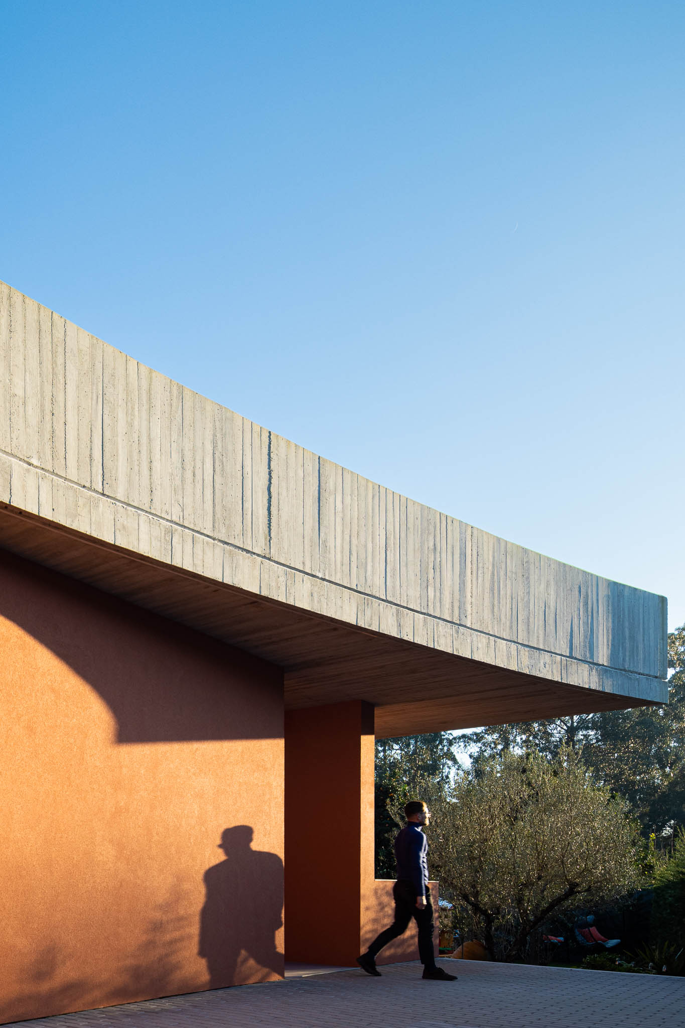 Exterior: Laje de betão aparente com forma curva e paredes cor de tijolo. — TM House arquitetura Inception Architects Studio em Santo Tirso