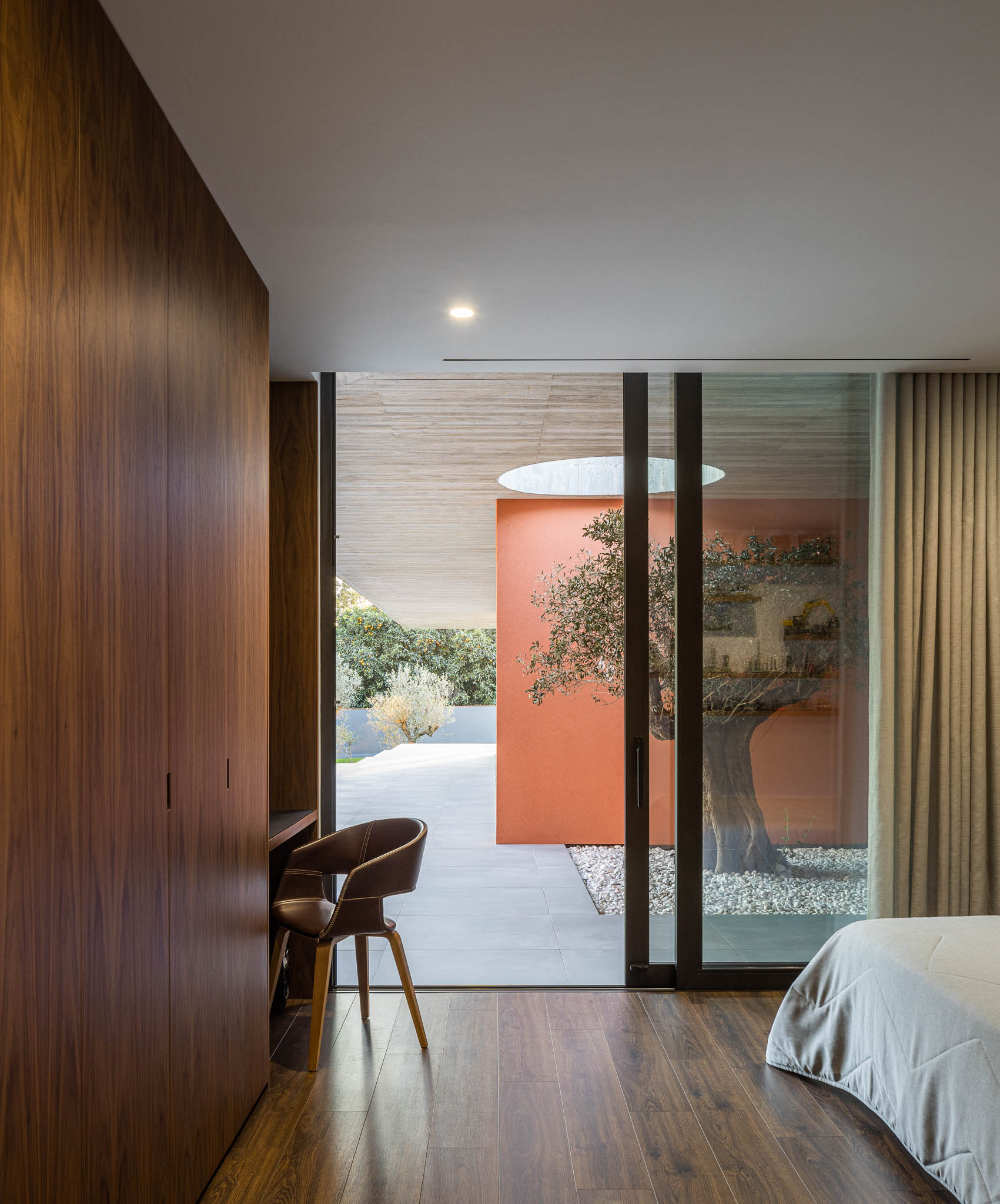 Quarto: Roupeiro em madeira, pavimento em madeira, vista para pátio interior com oliveira. — TM House arquitetura Inception Architects Studio em Santo Tirso