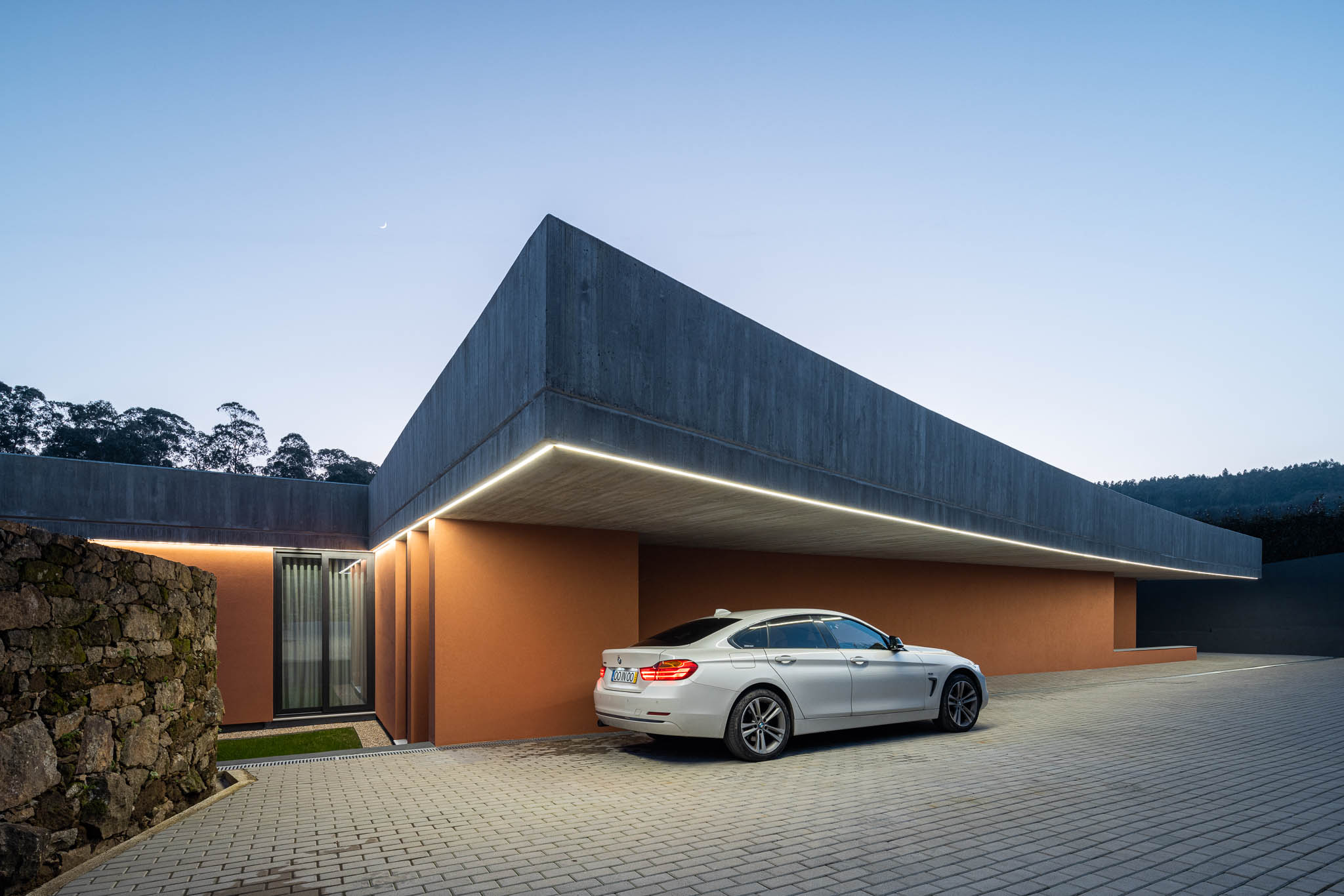 Exterior: Vista noturna da casa com laje de betão aparente e paredes cor de tijolo. — TM House arquitetura Inception Architects Studio em Santo Tirso