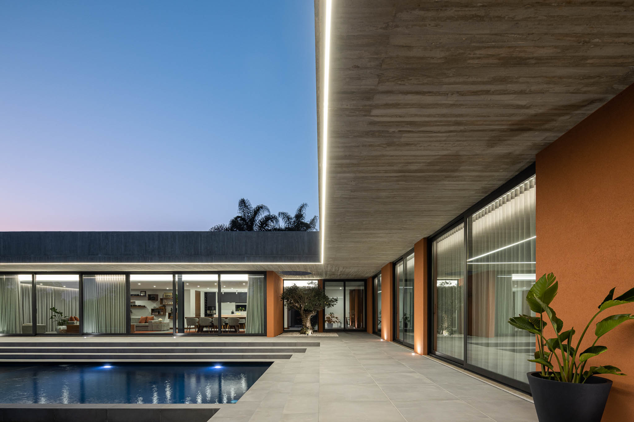 Exterior: Vista noturna da casa com piscina, laje de betão aparente e paredes cor de tijolo. — TM House arquitetura Inception Architects Studio em Santo Tirso