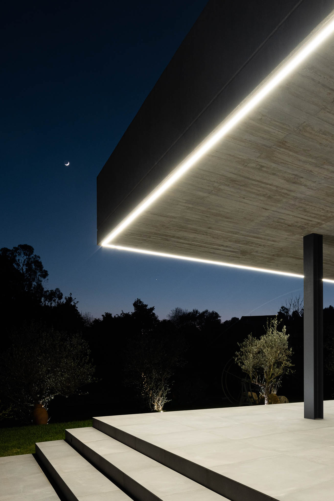 Exterior: Vista noturna do alpendre com laje de betão aparente e jardim. — TM House arquitetura Inception Architects Studio em Santo Tirso