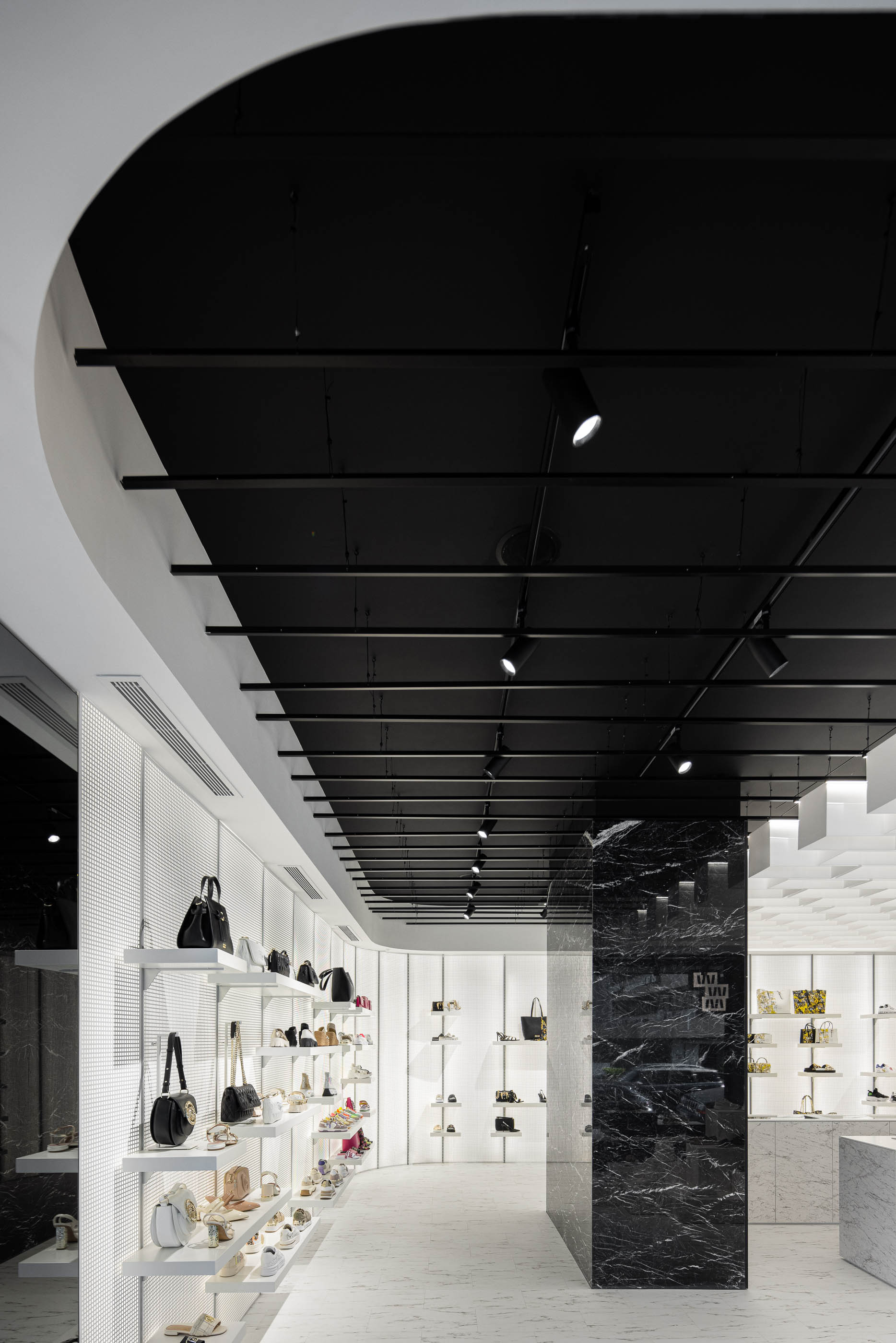 Loja: Corredor com prateleiras curvas, teto preto com candeeiros e coluna divisória em mármore preto. — Walk With Me Store arquitetura REM'A Arquitectos em Porto