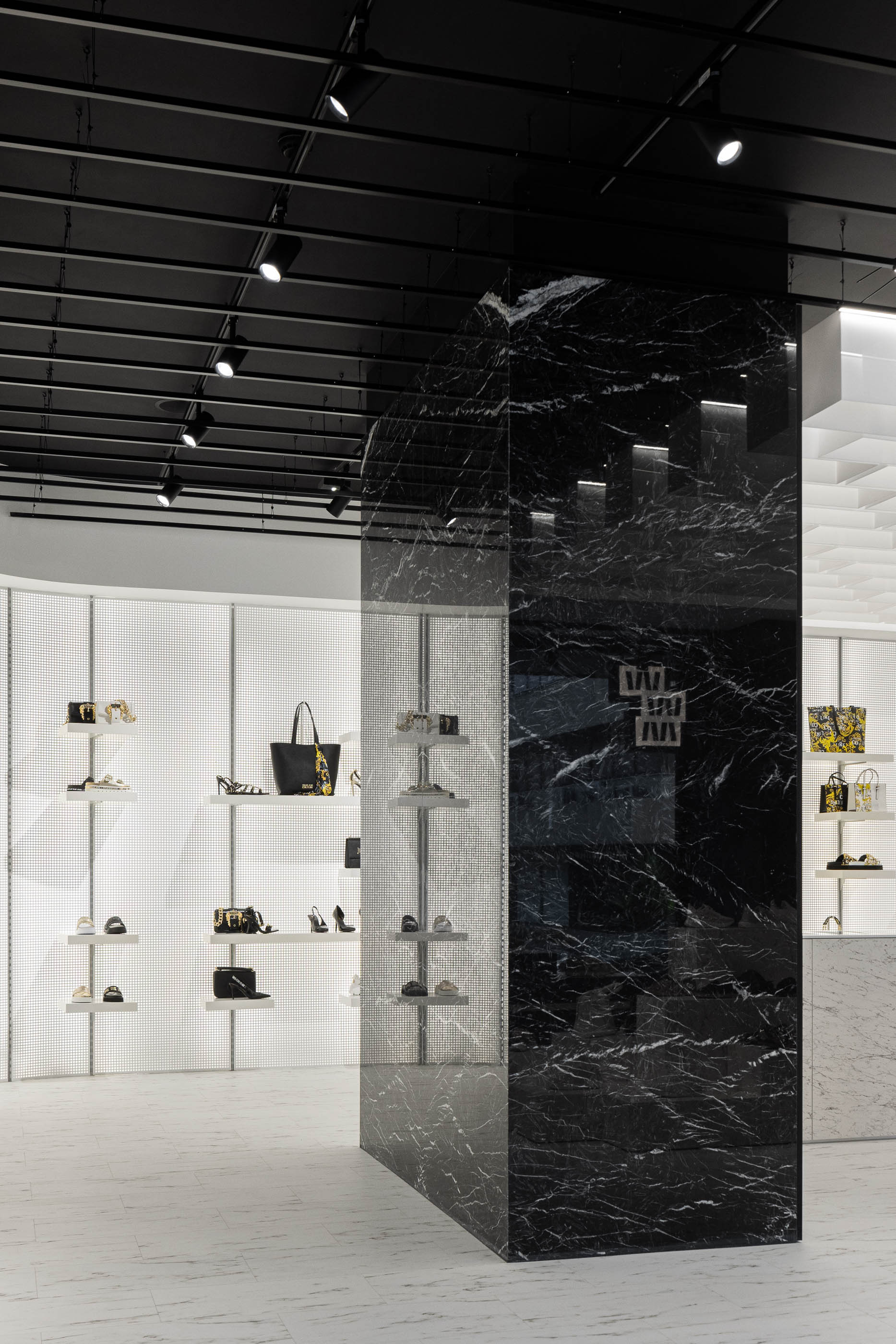 Loja: Coluna em mármore preto divide o espaço, com prateleiras iluminadas ao fundo e pavimento em mármore branco. — Walk With Me Store arquitetura REM'A Arquitectos em Porto
