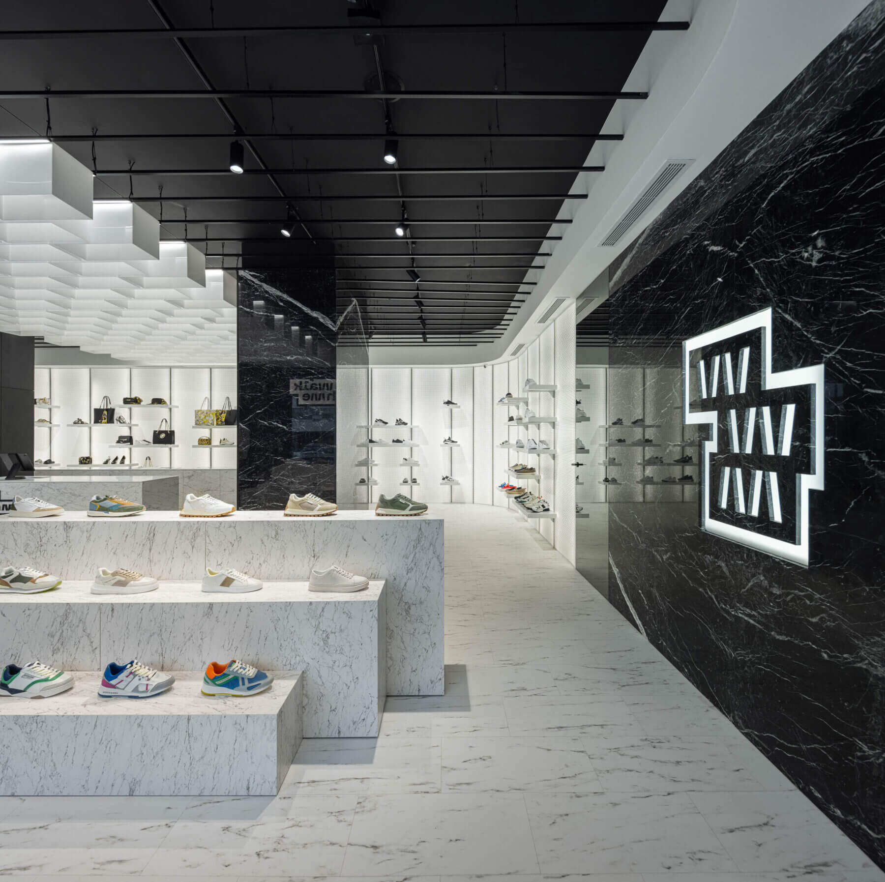 Loja: Expositores em mármore branco com calçado, parede em mármore preto com logótipo e teto com elementos geométricos. — Walk With Me Store arquitetura REM'A Arquitectos em Porto