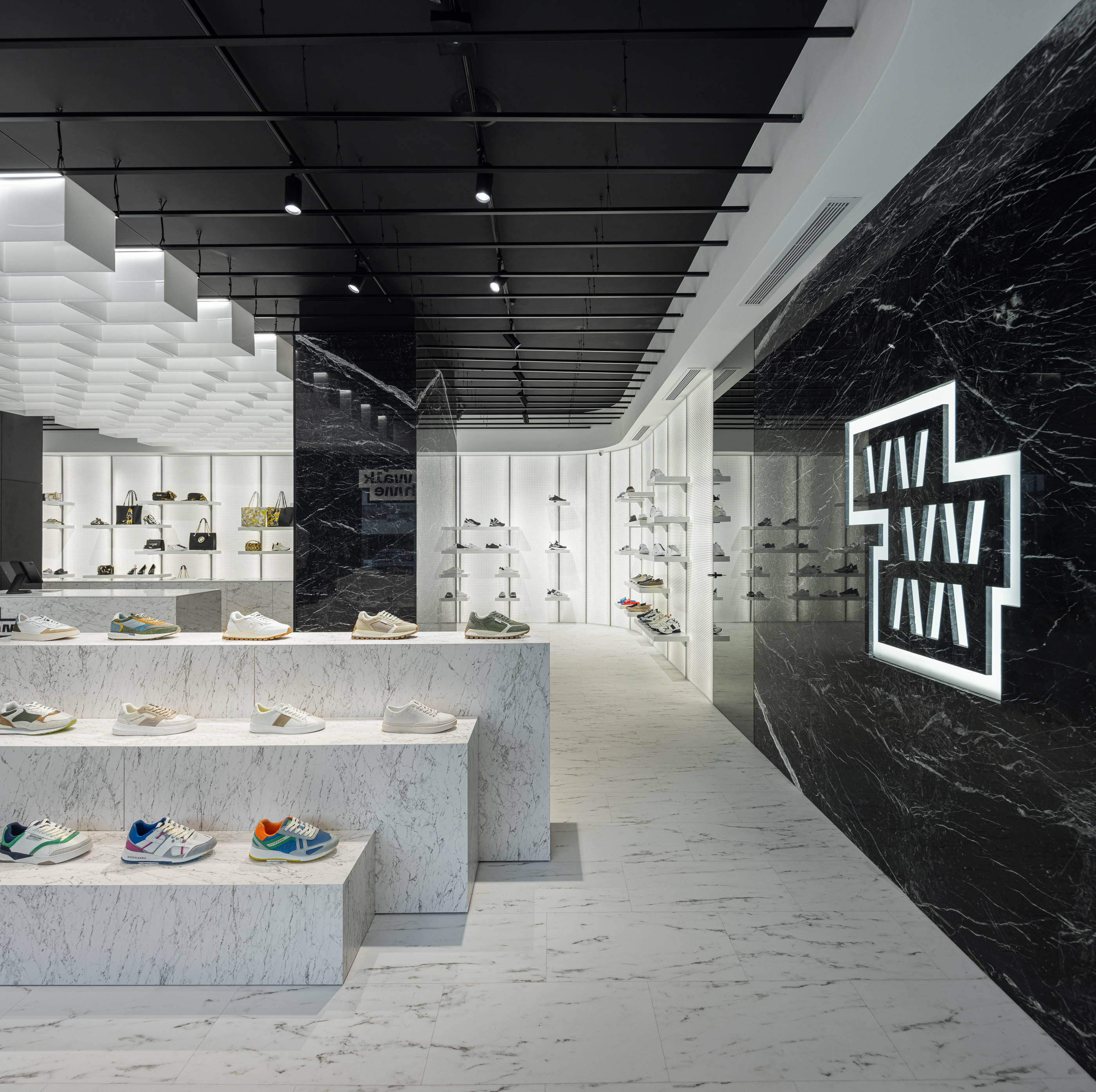 Loja: Expositores em mármore branco com calçado, parede em mármore preto com logótipo e teto com elementos geométricos. — Walk With Me Store arquitetura REM'A Arquitectos em Porto