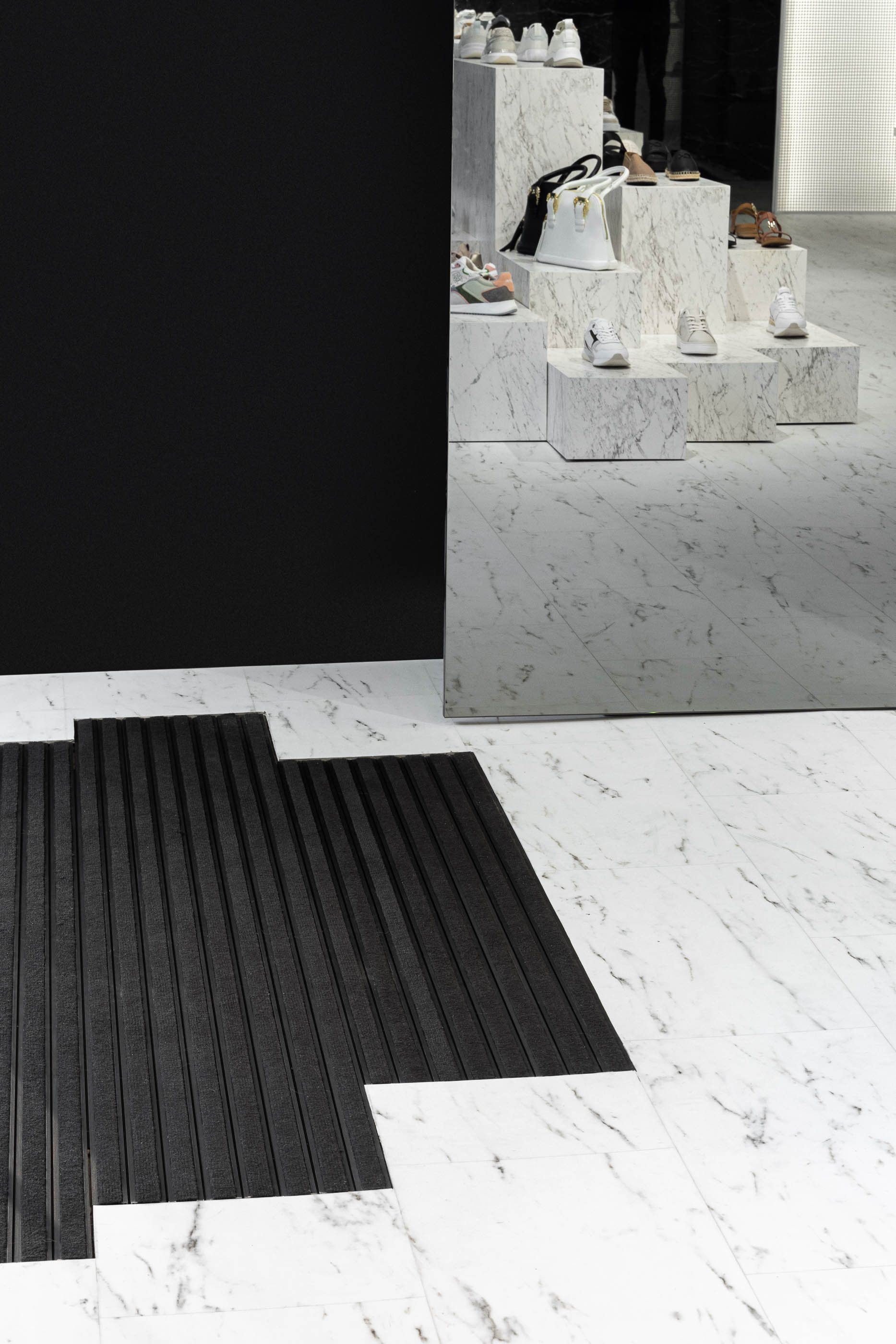 Loja: Detalhe do pavimento em mármore branco, tapete preto e expositores em mármore ao fundo. — Walk With Me Store arquitetura REM'A Arquitectos em Porto