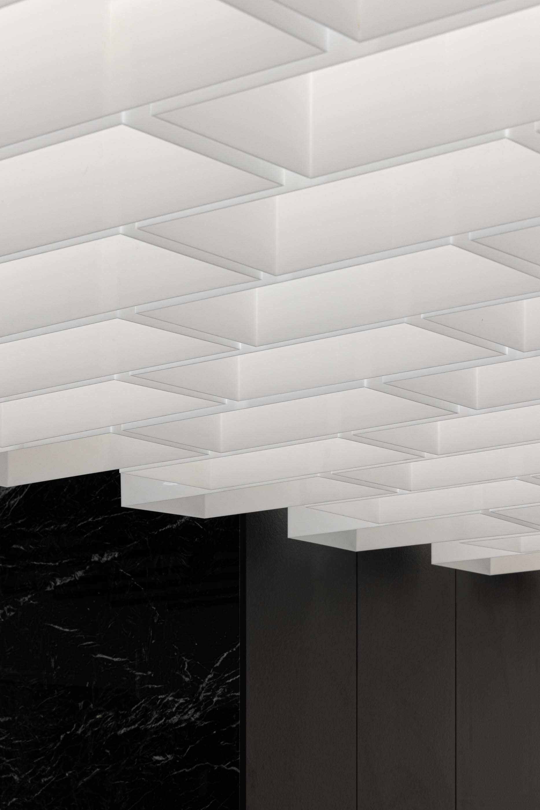 Teto: Detalhe do teto com elementos geométricos brancos e painel em mármore preto. — Walk With Me Store arquitetura REM'A Arquitectos em Porto