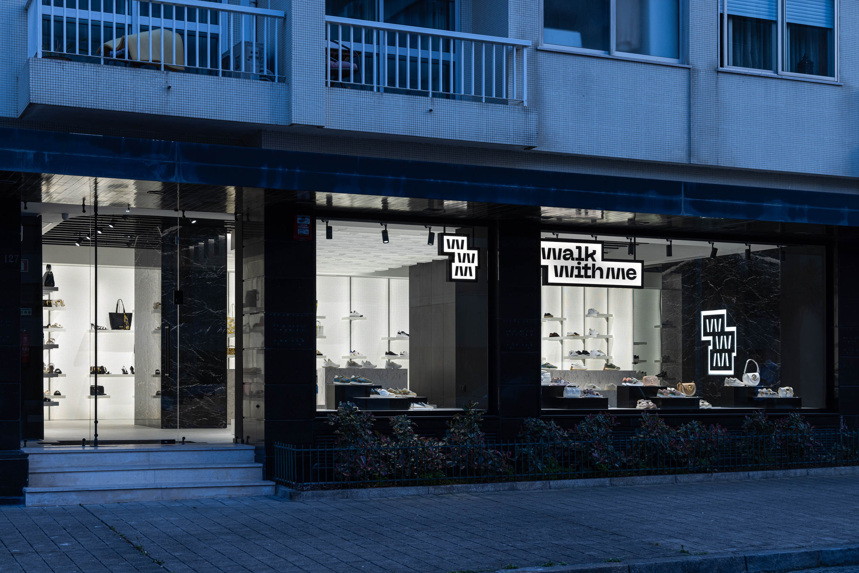 Fachada: Vista exterior da loja integrada no edifício, com montra e logótipos iluminados. — Walk With Me Store arquitetura REM'A Arquitectos em Porto