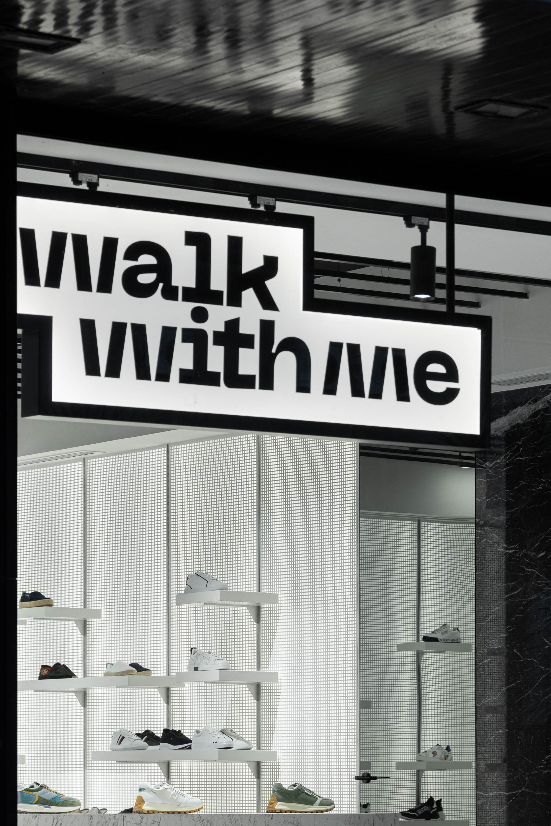 Fachada: Detalhe do logótipo iluminado sobre a montra e prateleiras com calçado. — Walk With Me Store arquitetura REM'A Arquitectos em Porto