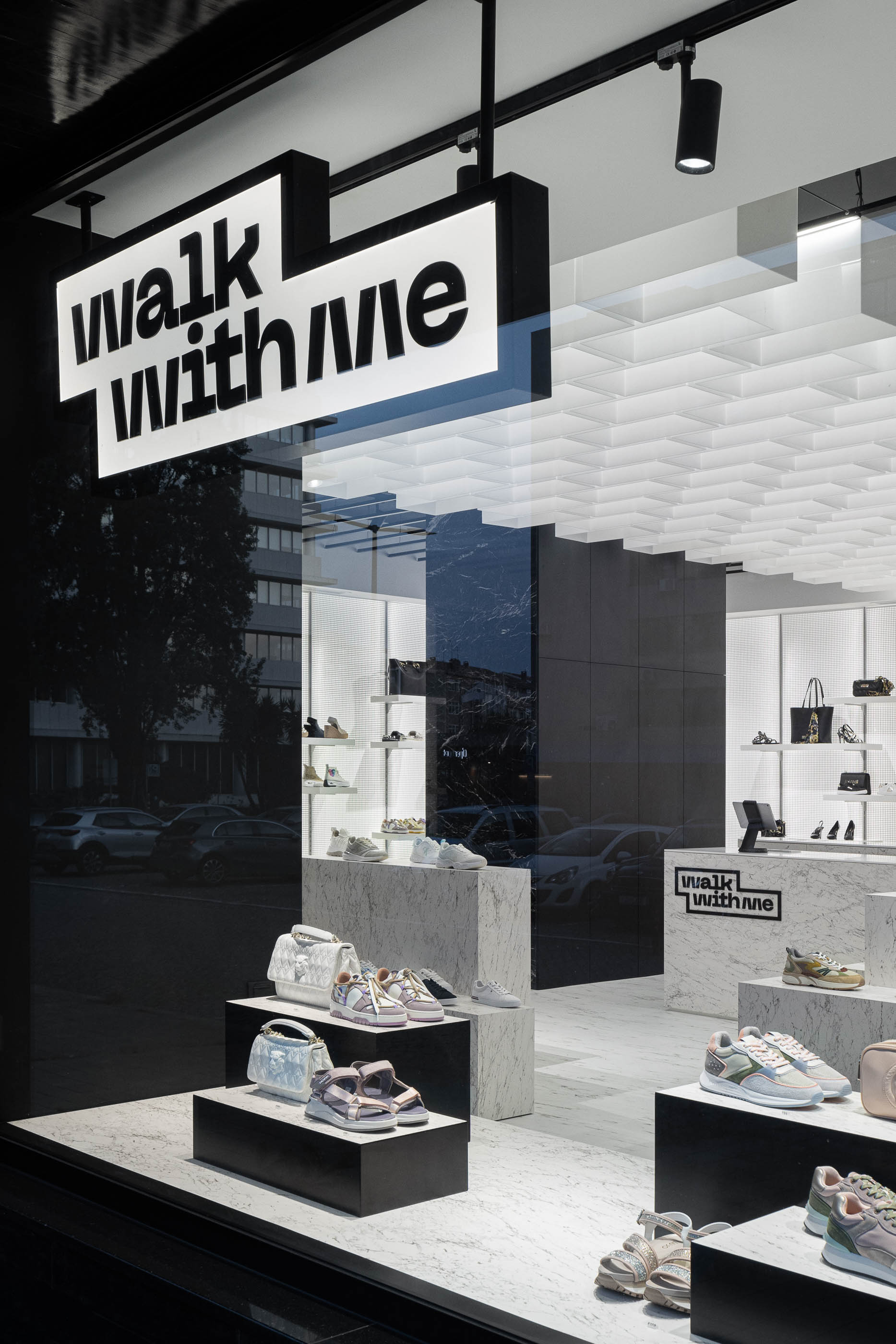 Fachada: Montra com calçado exposto em plataformas de mármore, sob logótipo iluminado e teto geométrico. — Walk With Me Store arquitetura REM'A Arquitectos em Porto