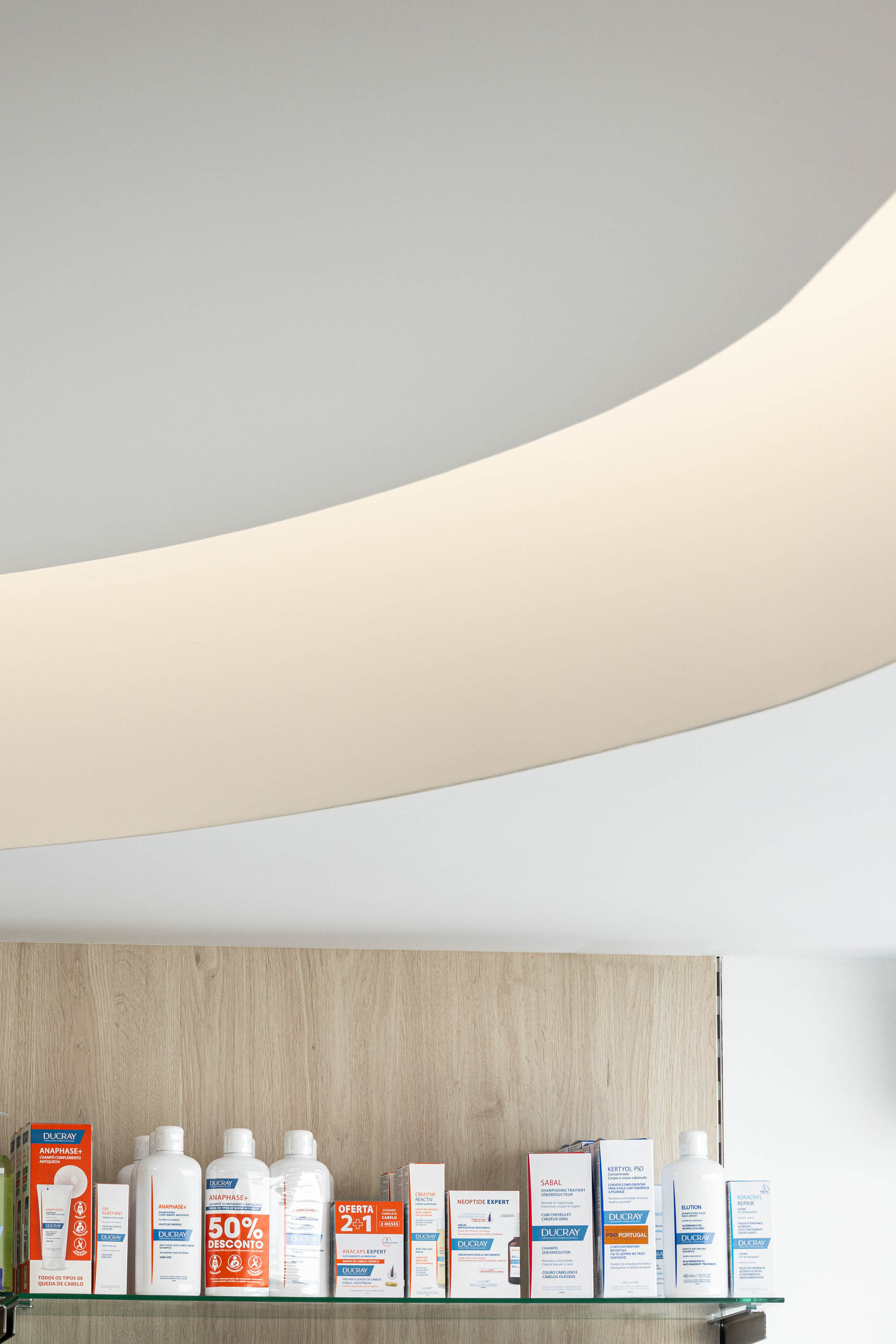 Teto: Detalhe do teto curvo com iluminação indireta e prateleiras com produtos. — Farmácia da Devesa arquitetura Tsou Arquitectos em Vila Nova de Famalicão