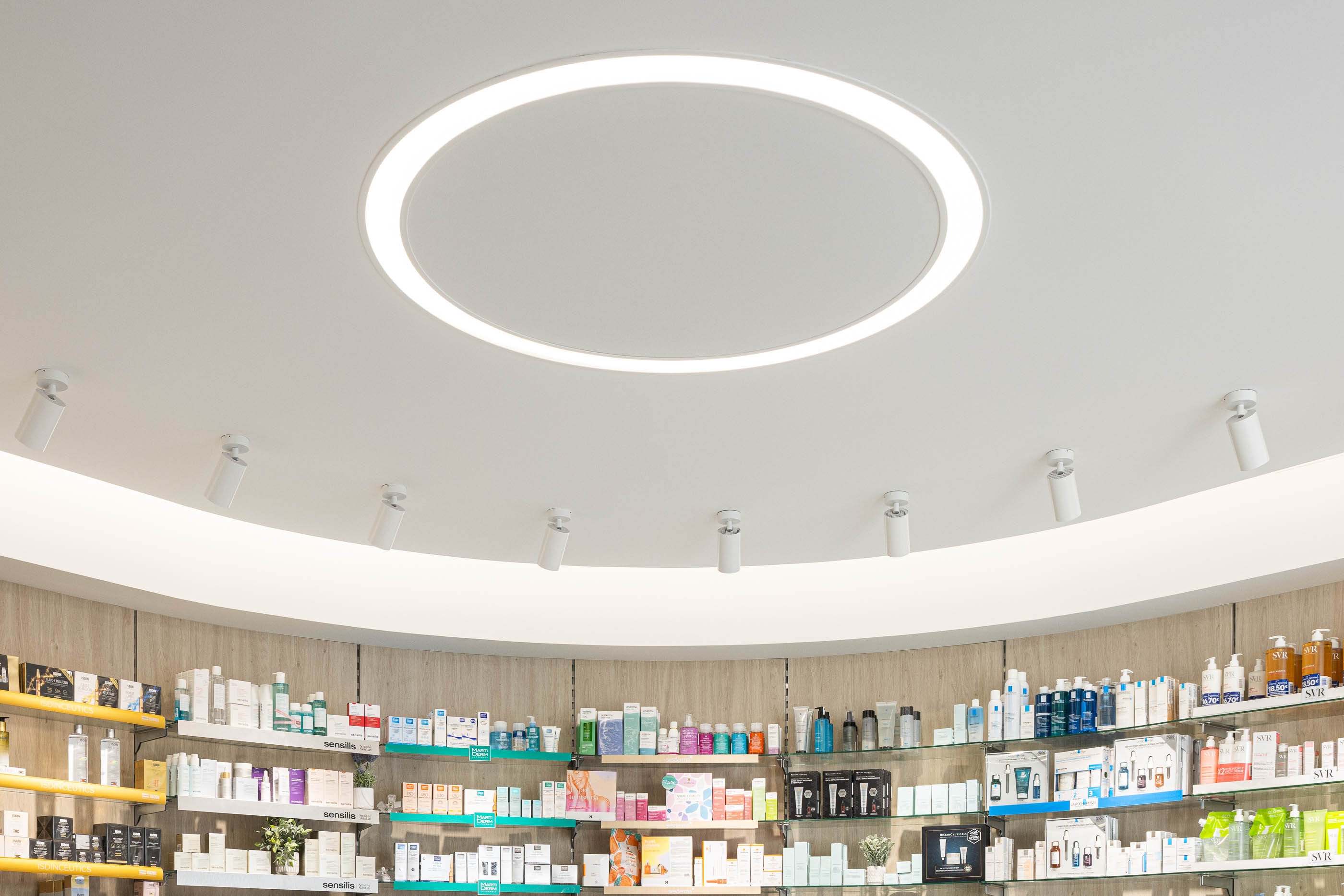 Teto: Candeeiro circular embutido no teto curvo, com projetores direcionáveis. — Farmácia da Devesa arquitetura Tsou Arquitectos em Vila Nova de Famalicão