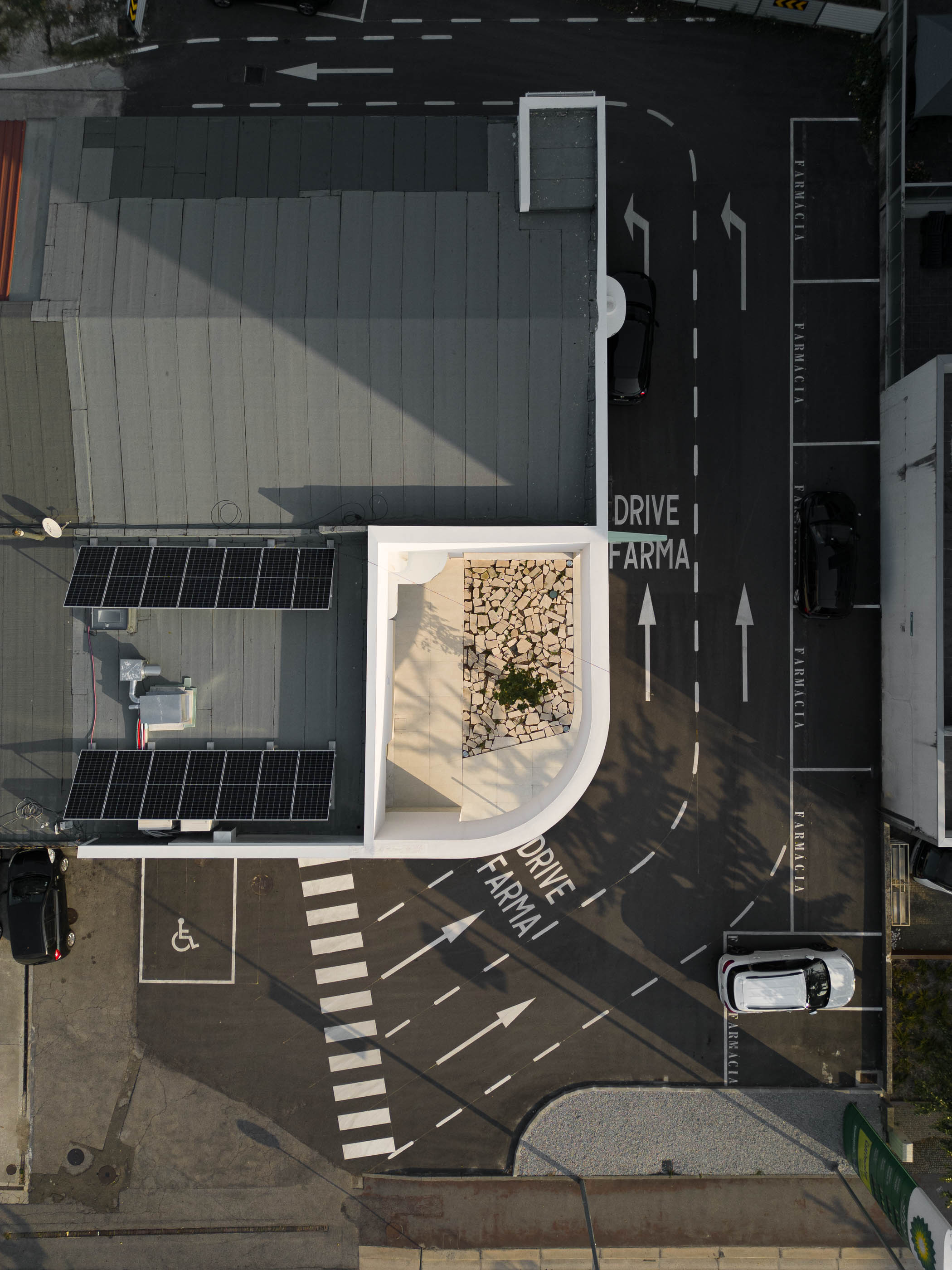 Cobertura: Vista aérea da farmácia com painéis solares, jardim interior e estacionamento com "Drive Farma". — Farmácia da Devesa arquitetura Tsou Arquitectos em Vila Nova de Famalicão
