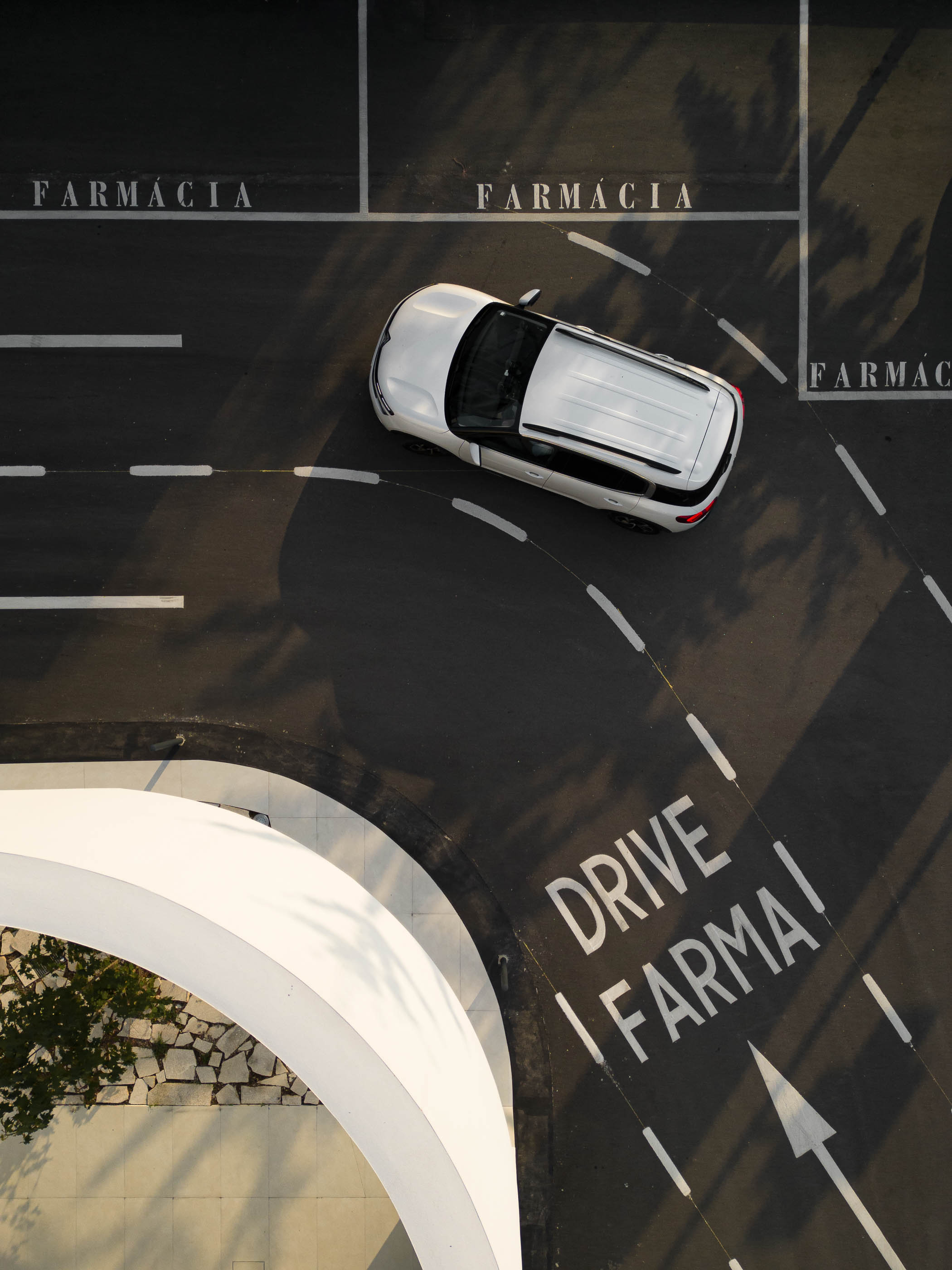 Estacionamento: Vista aérea do estacionamento com sinalização "Drive Farma" e carro a circular. — Farmácia da Devesa arquitetura Tsou Arquitectos em Vila Nova de Famalicão