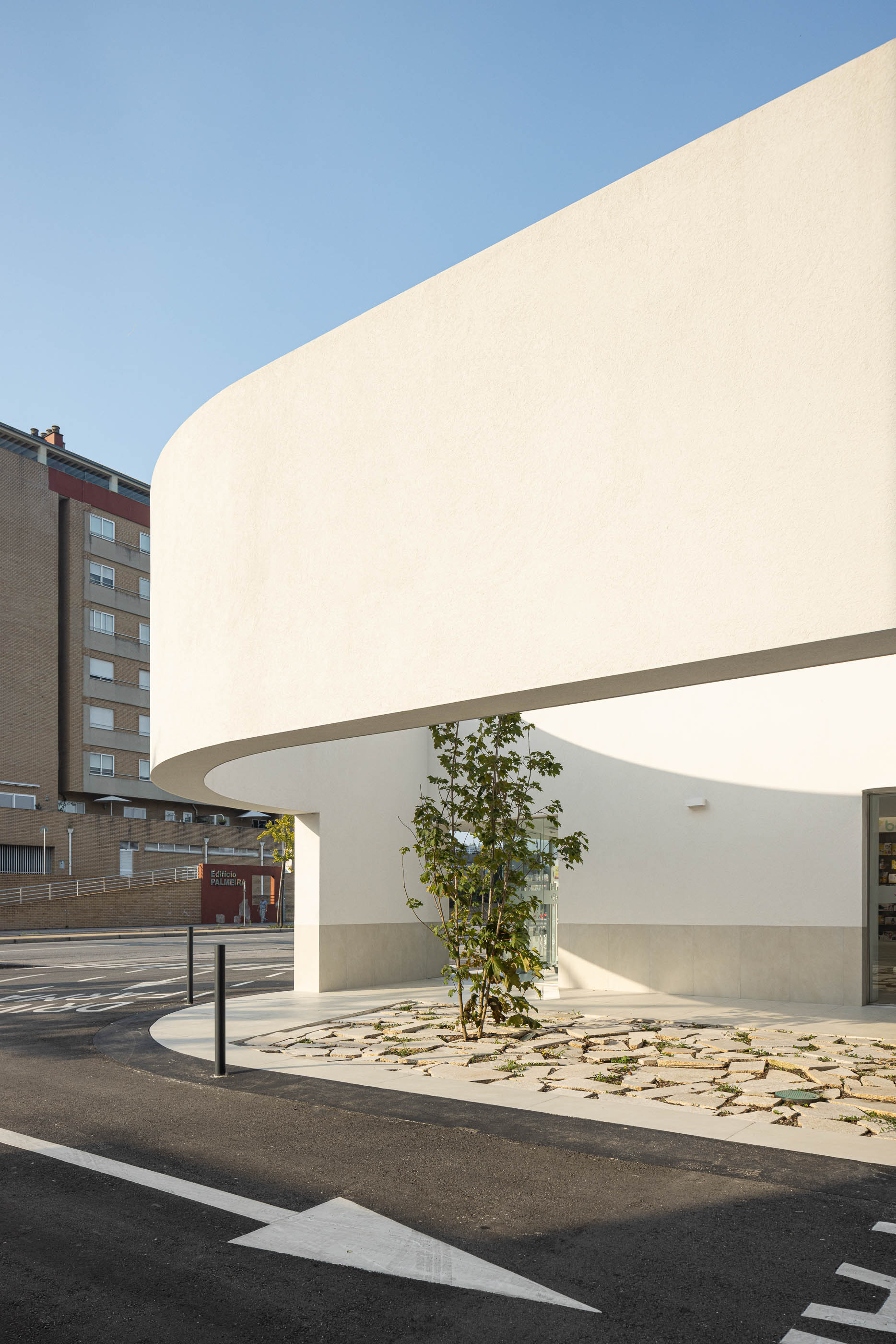Exterior: Fachada curva branca com jardim interior e estacionamento. — Farmácia da Devesa arquitetura Tsou Arquitectos em Vila Nova de Famalicão